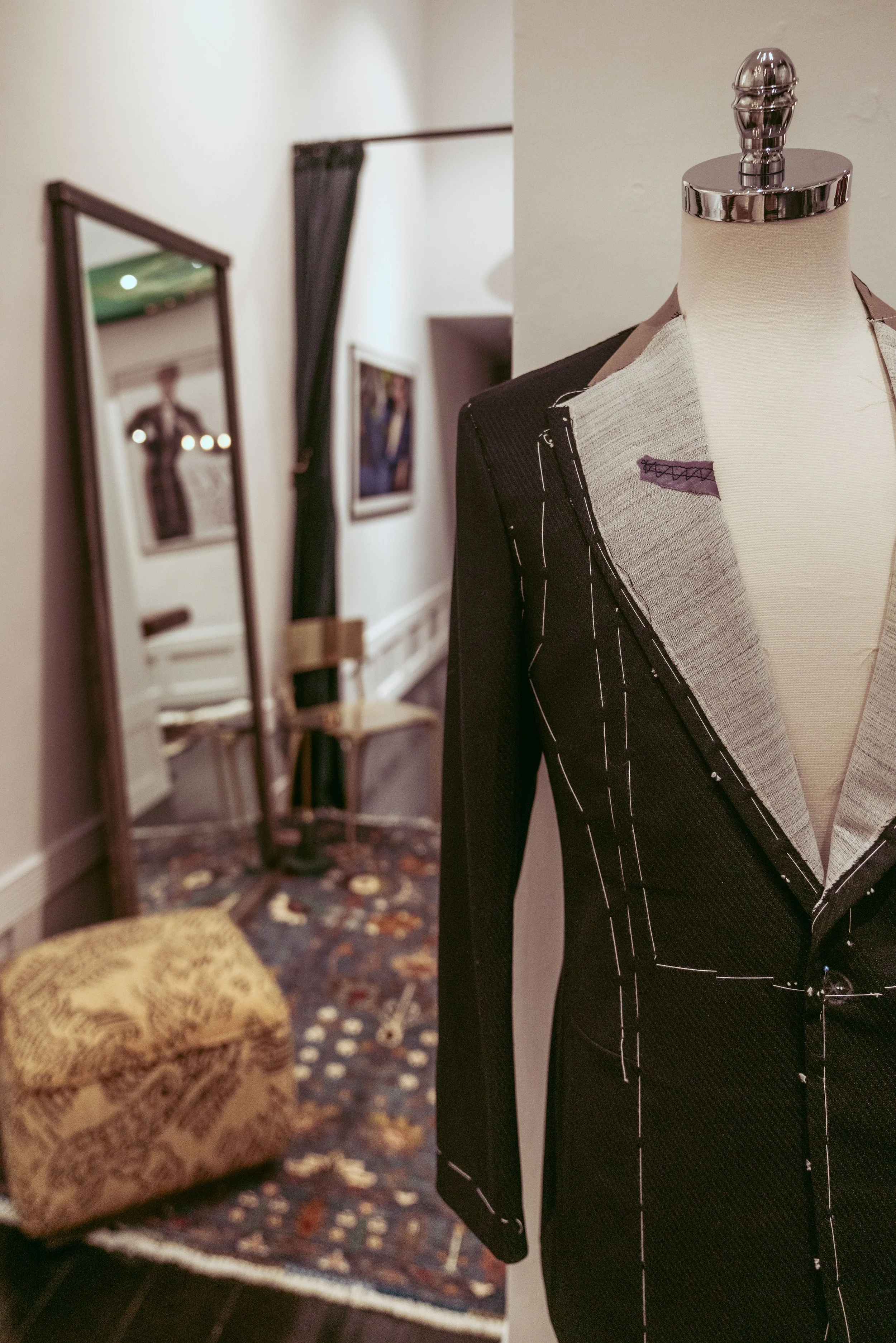 Inside the Scarborough Custom Tailoring showroom in San Francisco is a close-up of a dress form mannequin with black and beige fabric on it, located in a room with framed photos on the wall and a patterned carpet.