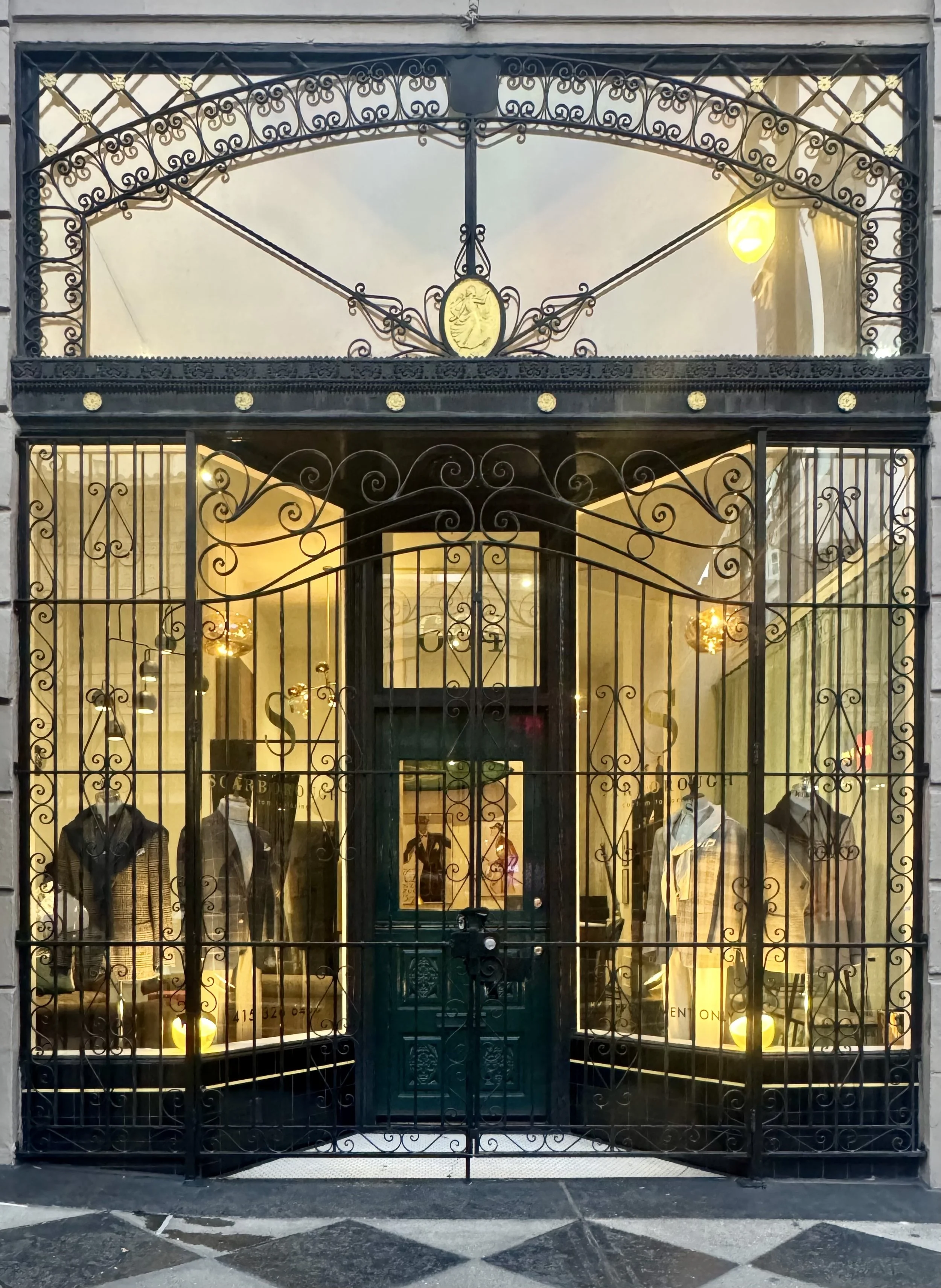 Scarborough Custom Tailoring storefront in San Francisco with intricate black wrought-iron gates in front, showcasing mannequins dressed in men's clothing inside a well-lit interior.