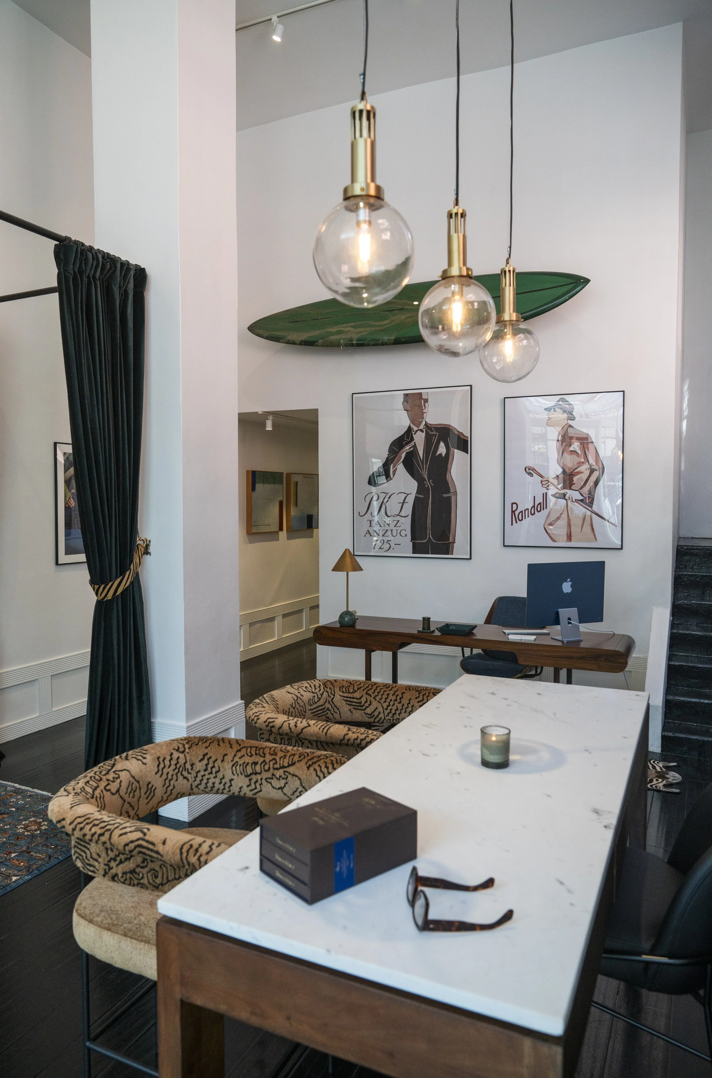 A modern interior space with a white marble table, patterned chairs, pendant lights, hung art, a laptop, glasses, and a candle on the table.