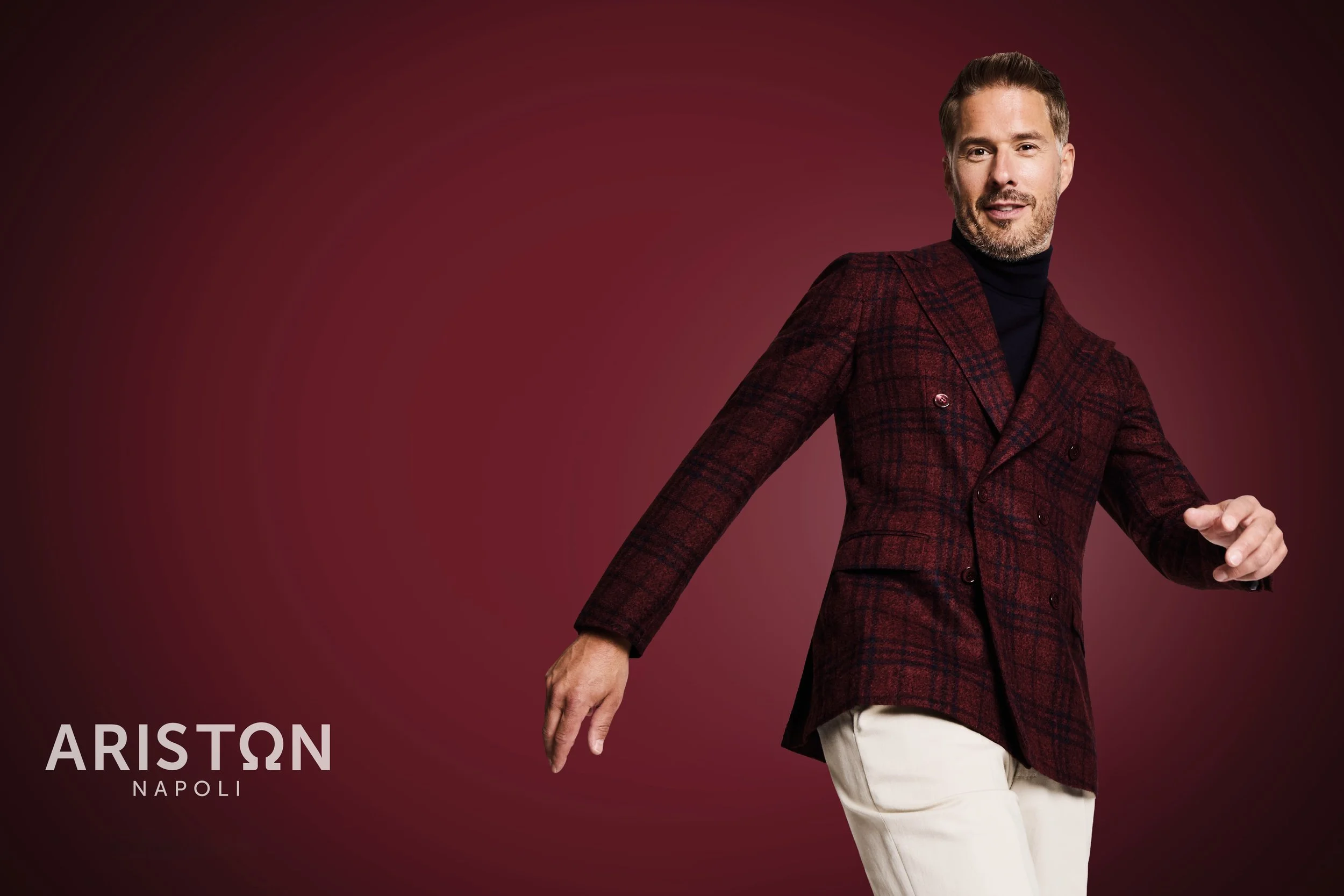 Man in a maroon plaid blazer and beige pants posing against a maroon background, with the text "ARISTON NAPOLI" at the bottom left.