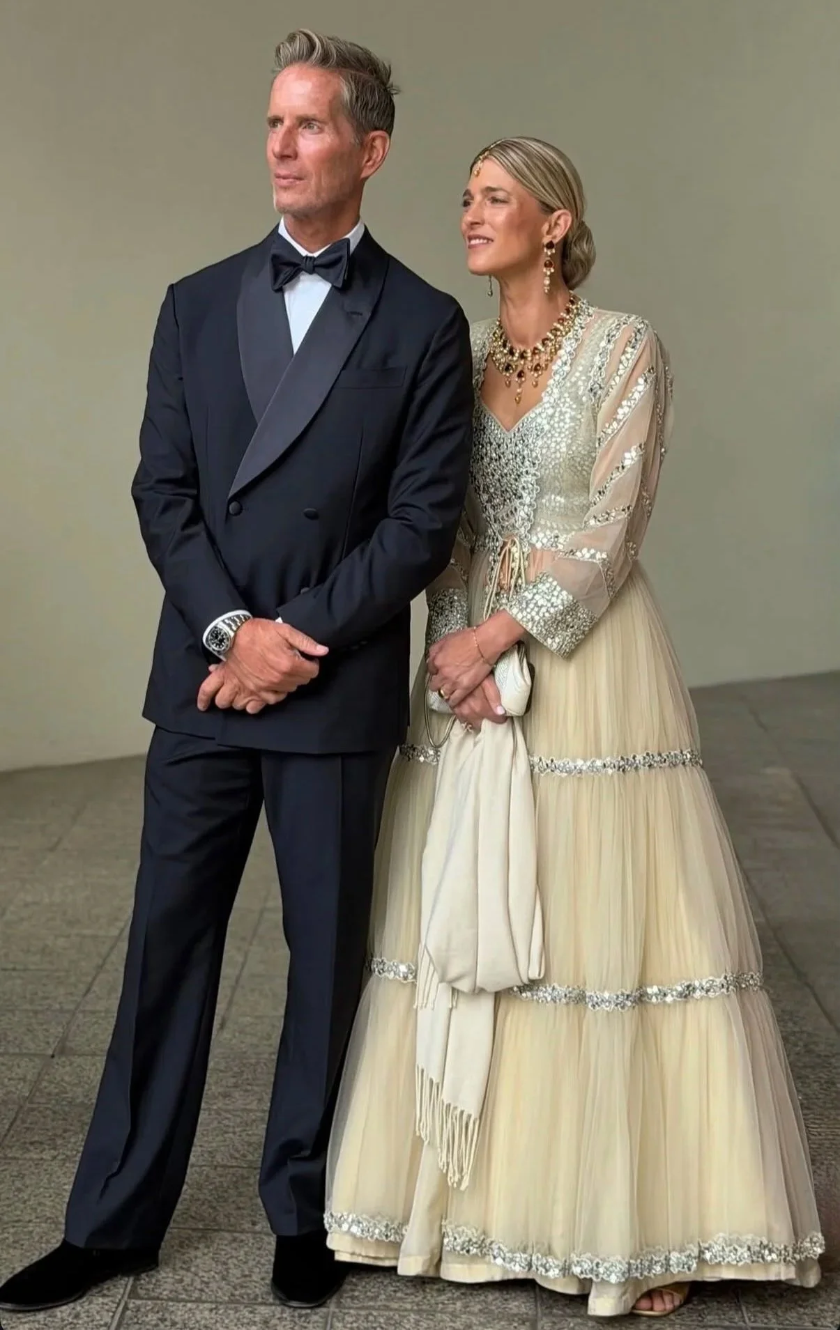 Christian wearing a Scarborough tuxedo standing next to a woman in an ornate cream-colored gown, both dressed elegantly for a formal event.