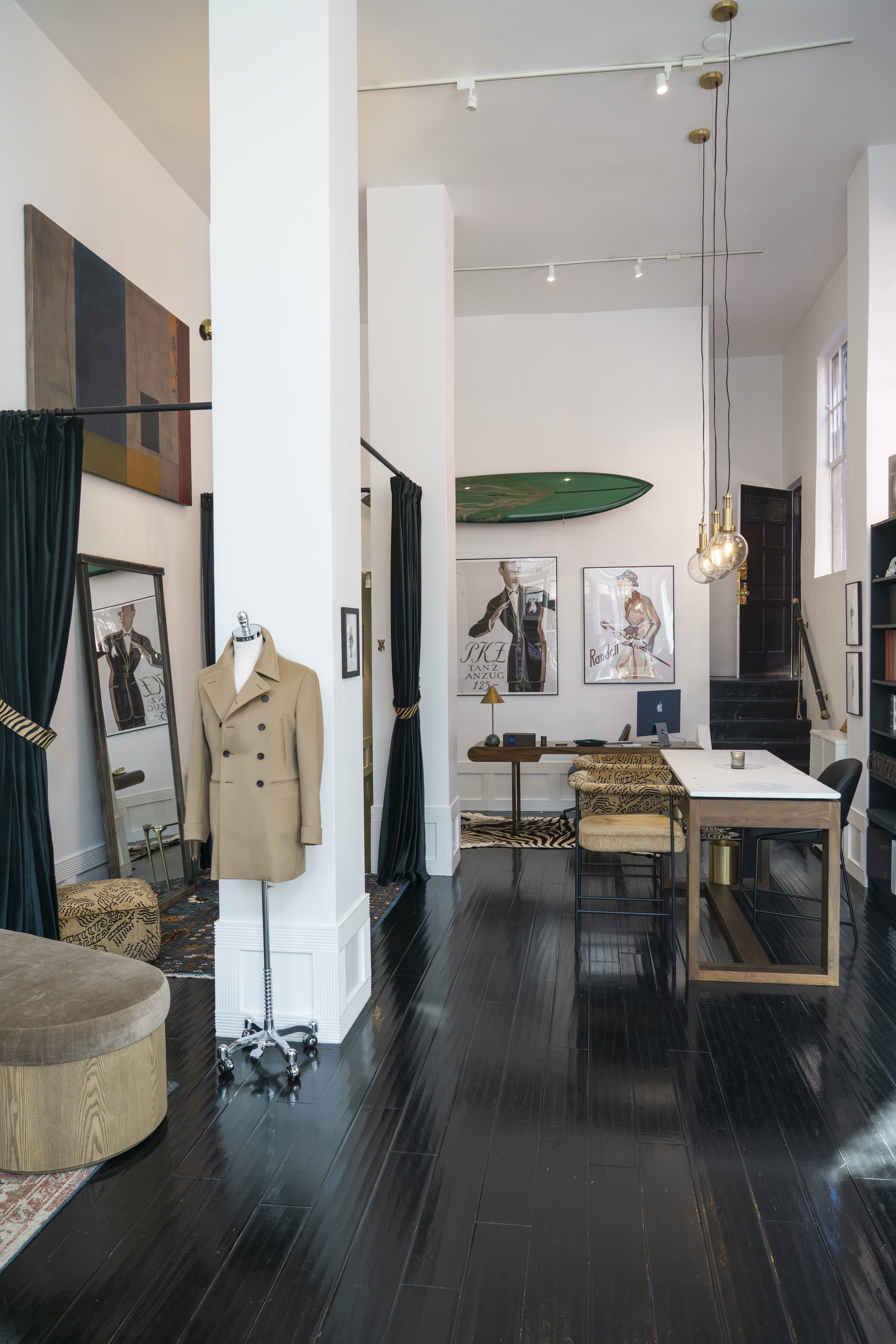 Interior of the showroom with various art pieces and decor, featuring white walls, dark wooden floors, a beige coat on a dress form, and a mixture of contemporary and vintage furniture.