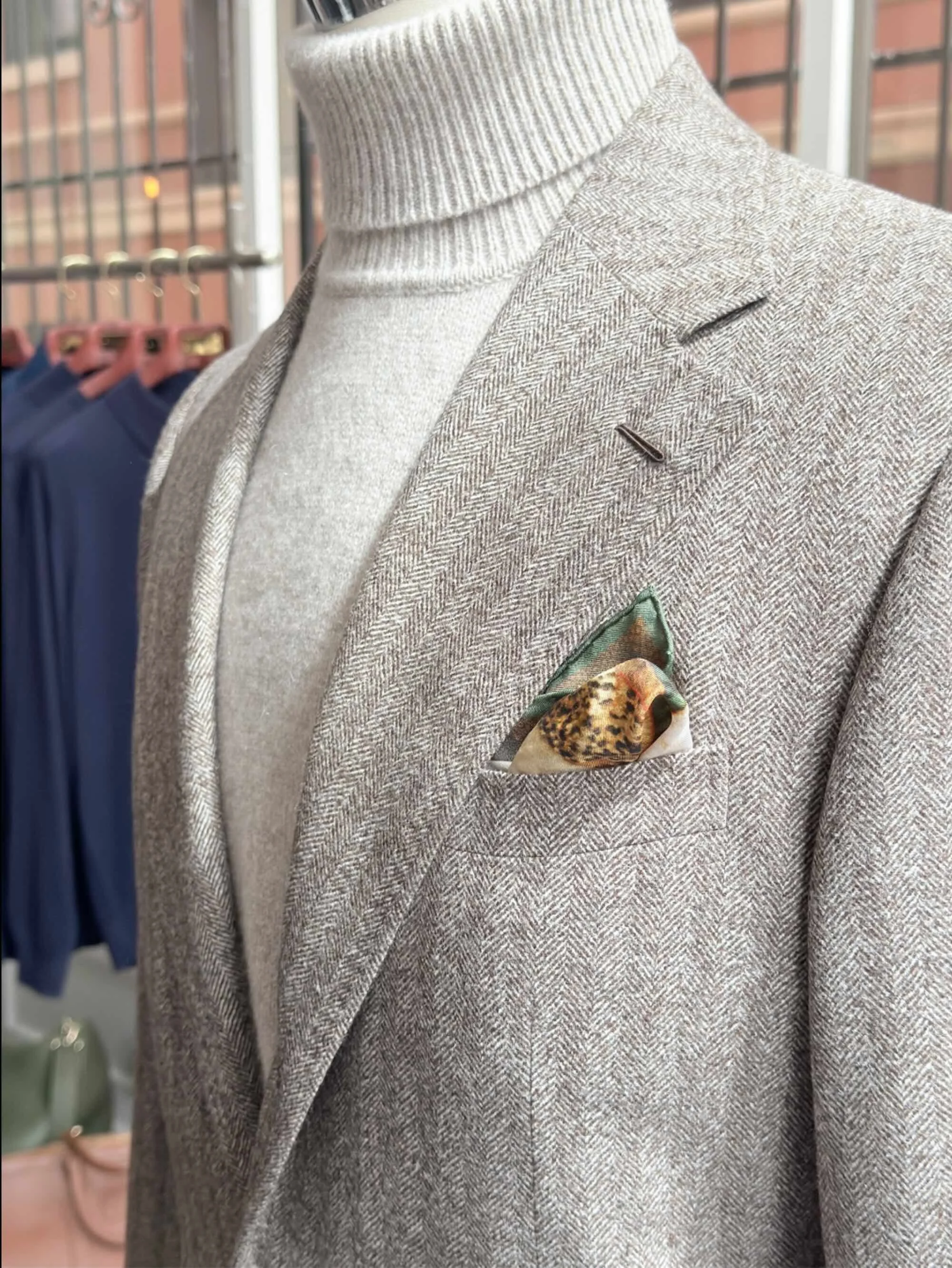 Close-up of a Scarborough custom gray herringbone sport coat with notch lapel, lapel buttonhole and printed silk pocket square, worn over a cream turtleneck.