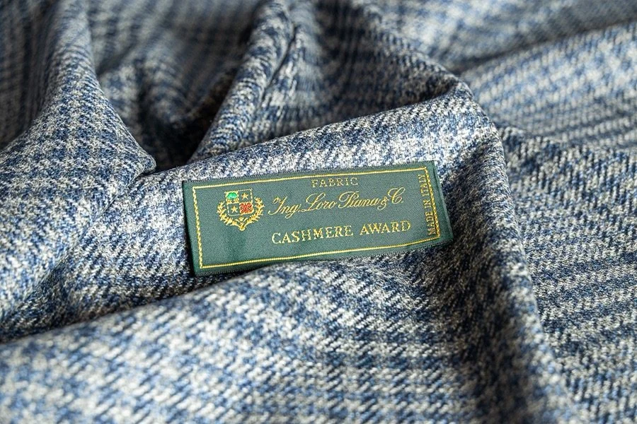 Close-up of a Loro Piana blue and gray cashmere fabric with a green label that reads 'Cashmere Award' attached to the material.