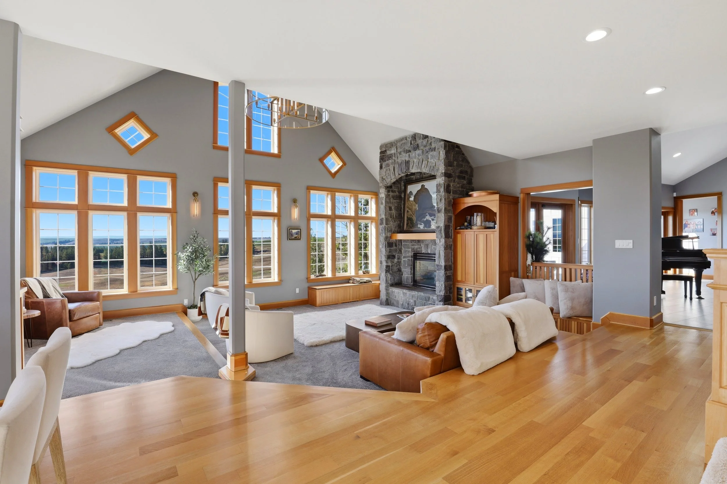 Spacious living room with large windows, a stone fireplace, and mixed furniture including sofas and chairs, with a view of countryside outside.