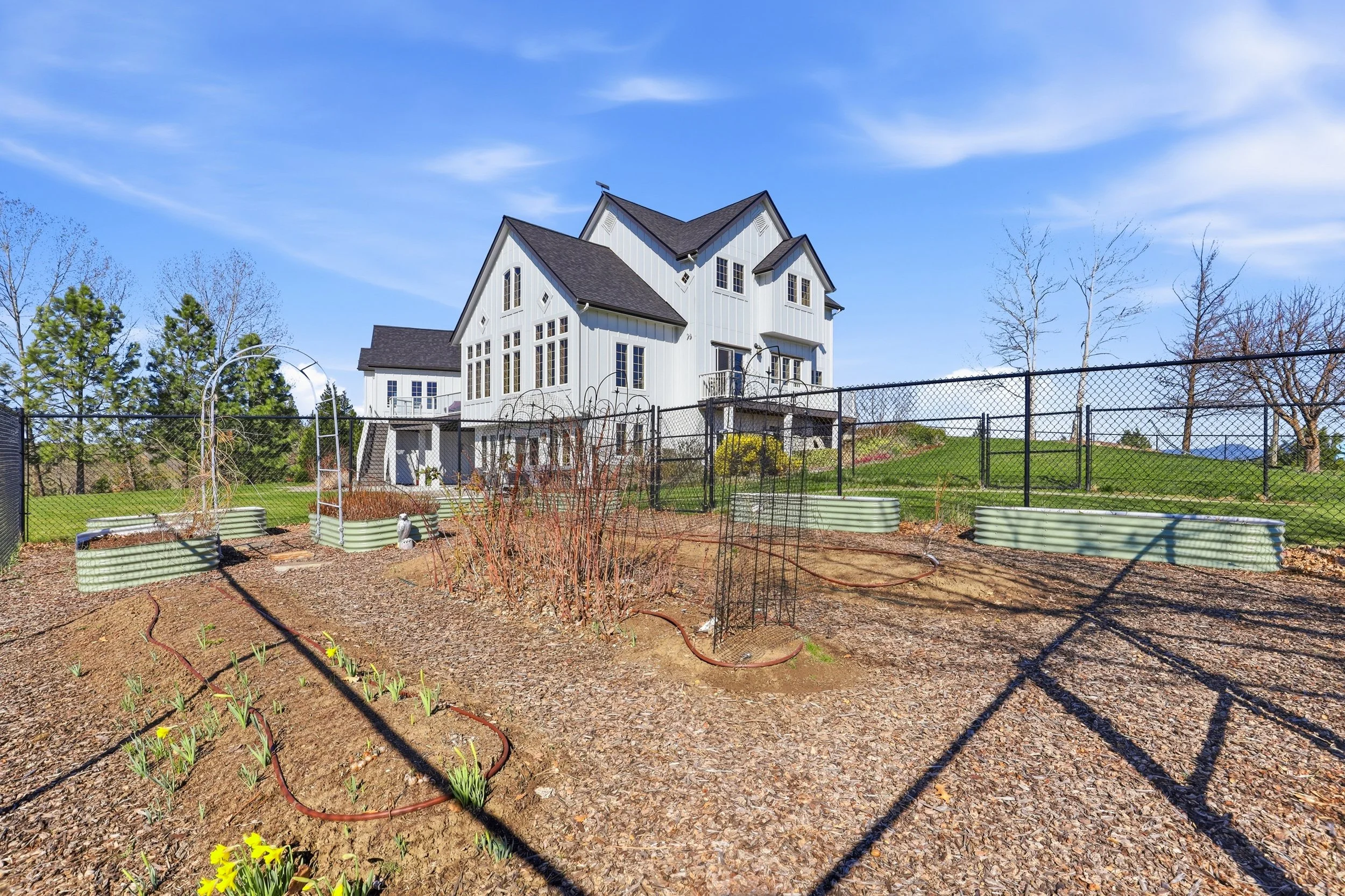 A backyard with a garden and a white house in the background under a bright blue sky