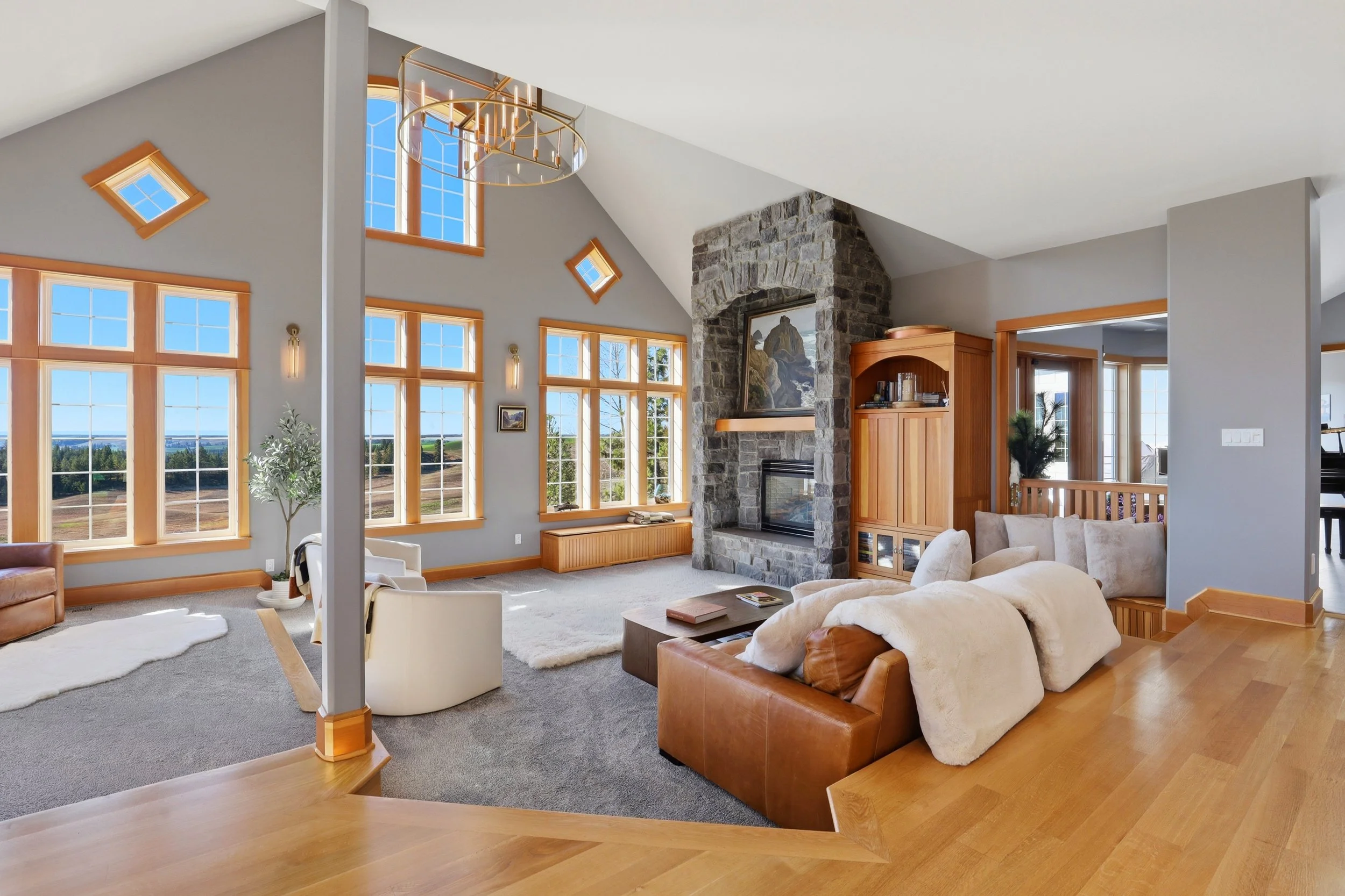 Bright living room with large windows, a stone fireplace, beige and brown furniture, and a view of the outdoors.