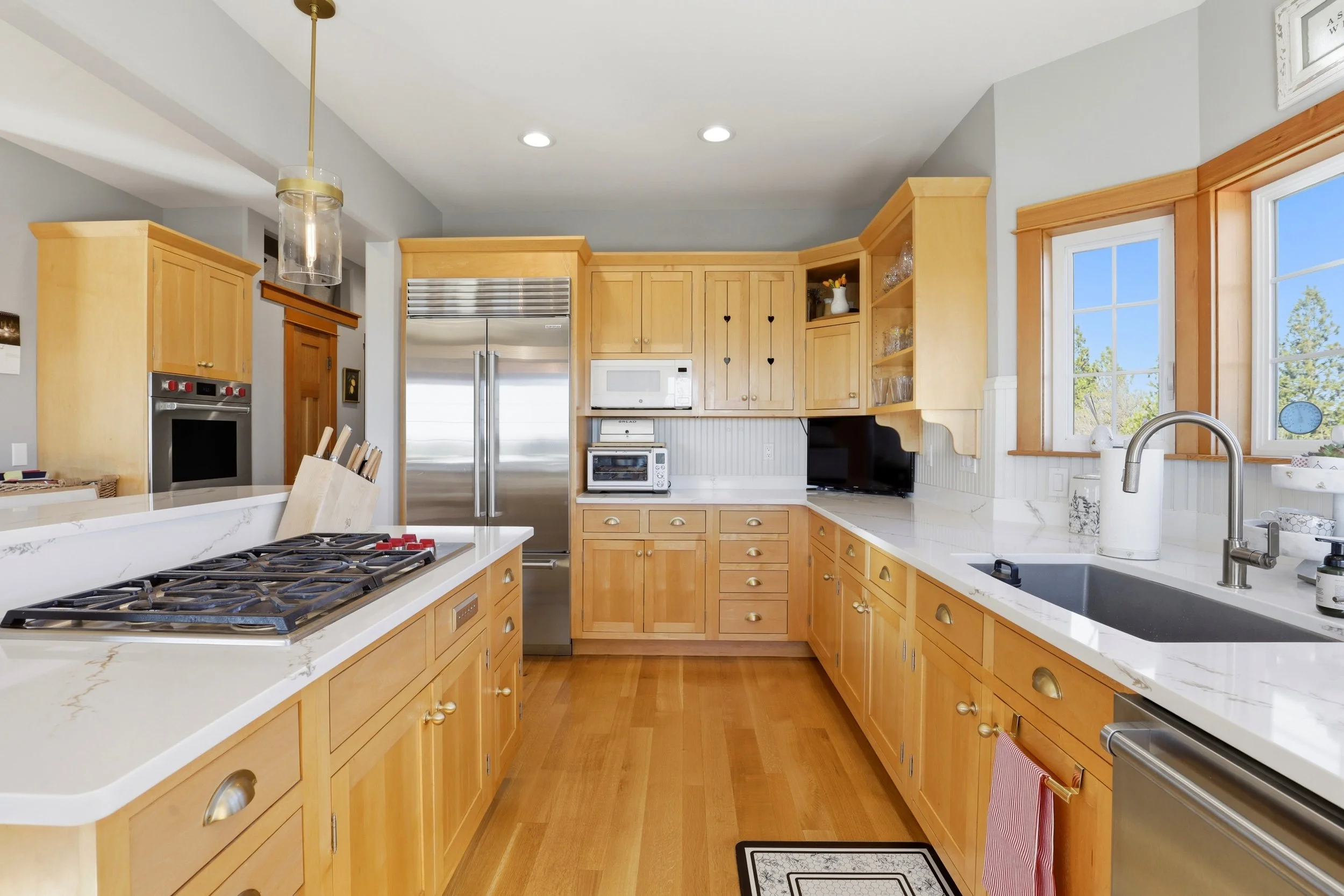 A bright kitchen with wooden cabinets, white countertops, stainless steel appliances, a gas stove, and large windows letting in natural light.