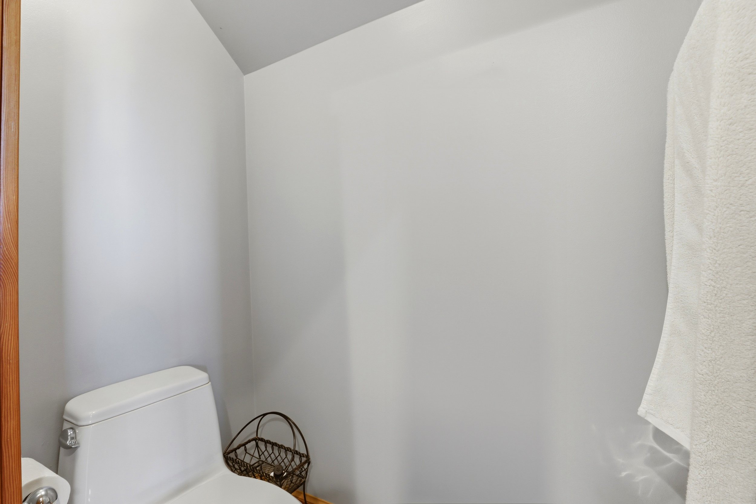 Small bathroom with a white toilet, a wicker basket, a bath towel, and plain white walls with a sloped ceiling.
