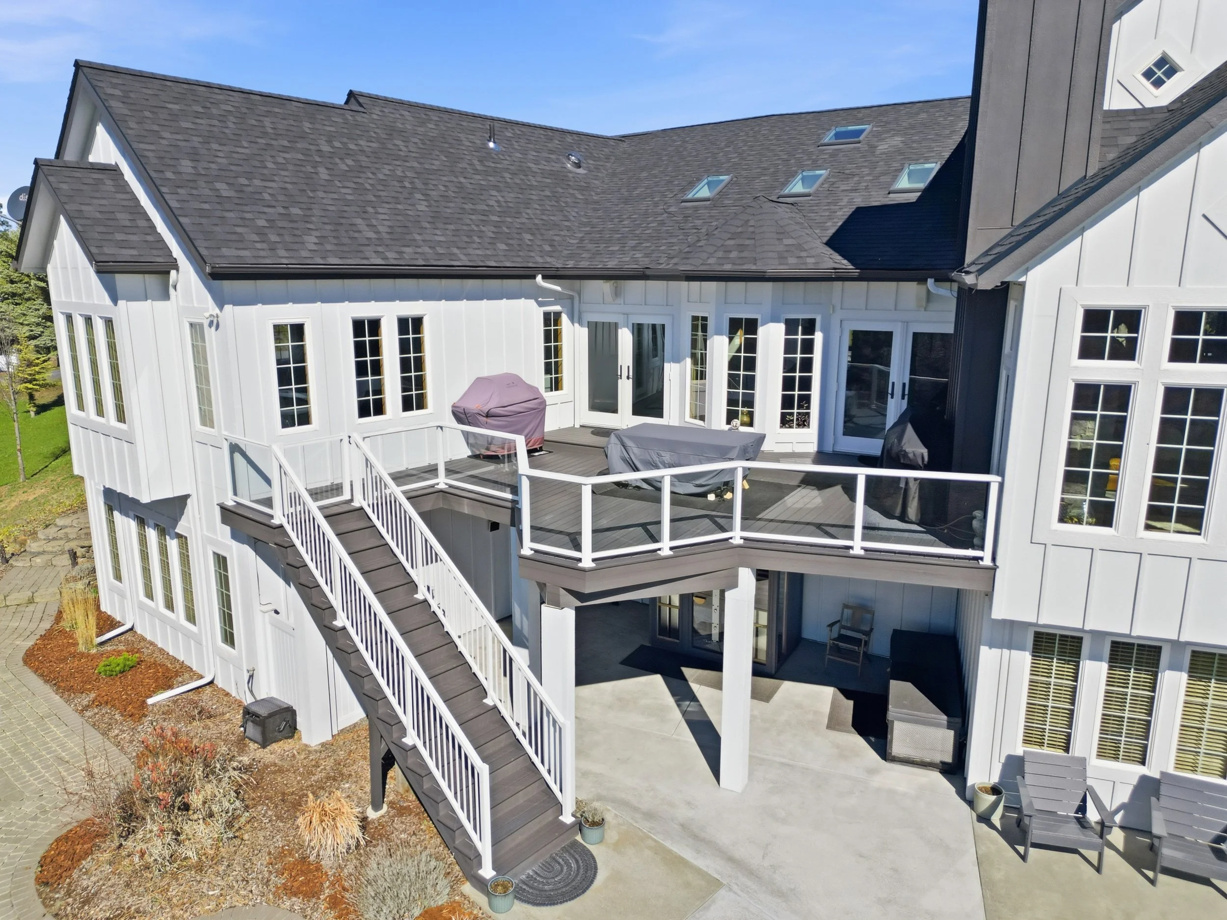 Backyard with a deck, outdoor furniture, and a multi-story house with large windows and skylights.