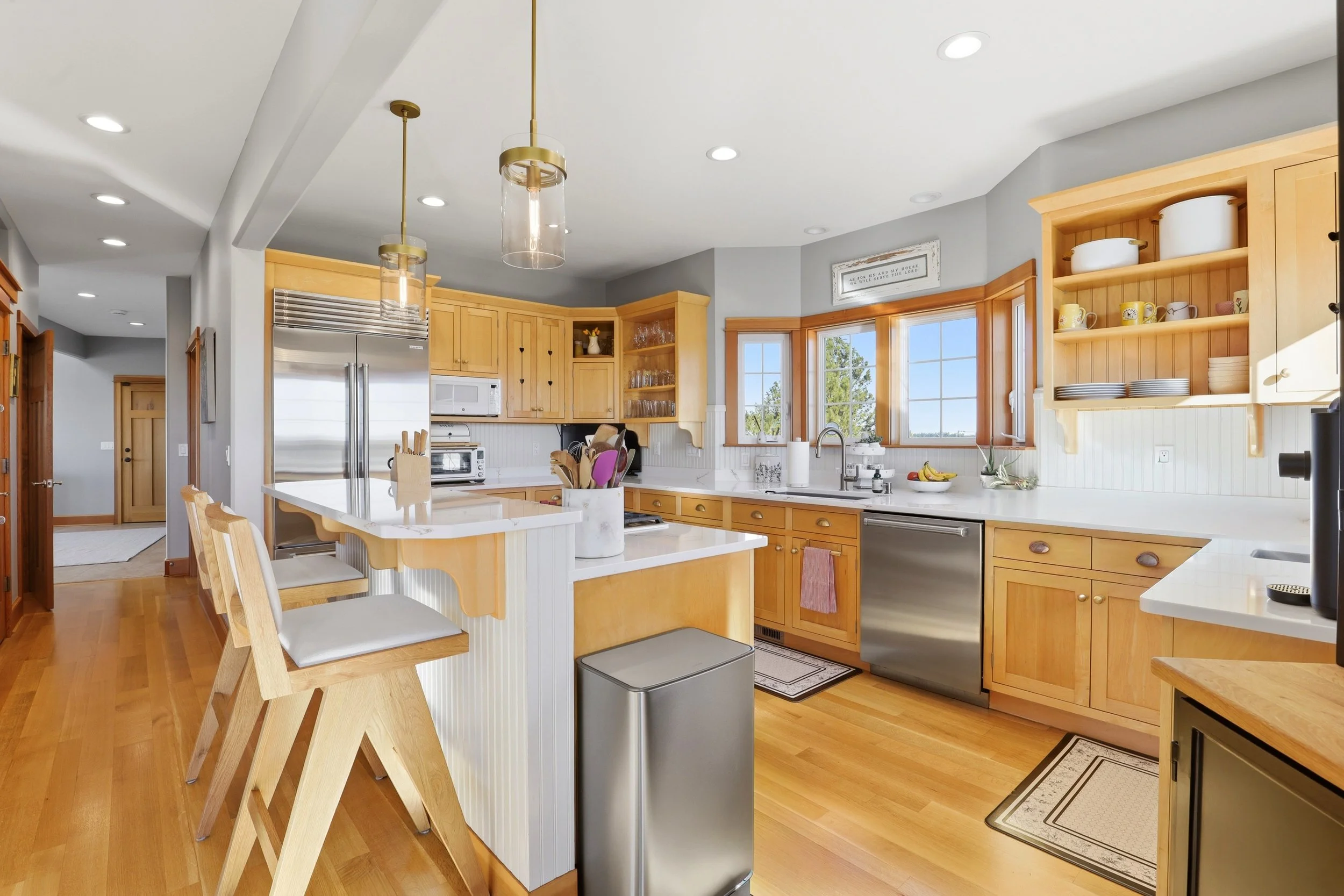 A modern kitchen with wooden cabinets, a white island, stainless steel appliances, a sink by a window, and hanging pendant lights.