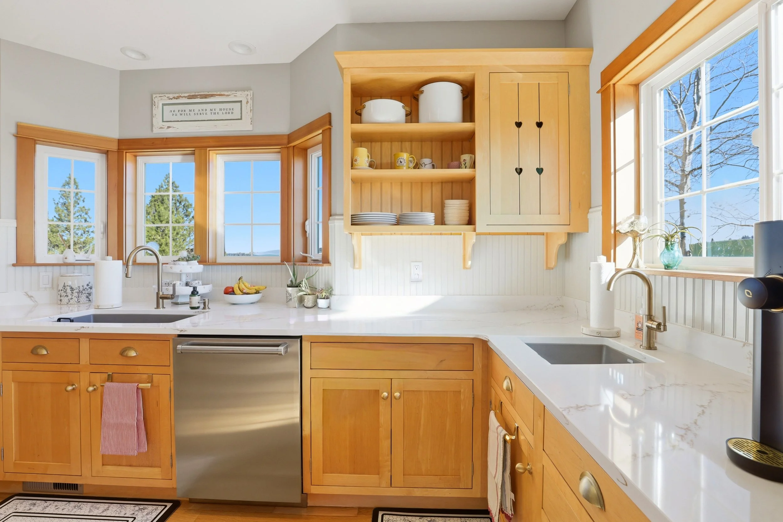 Bright kitchen with natural light, featuring wooden cabinets, a marble countertop, and a window view of trees and a blue sky.