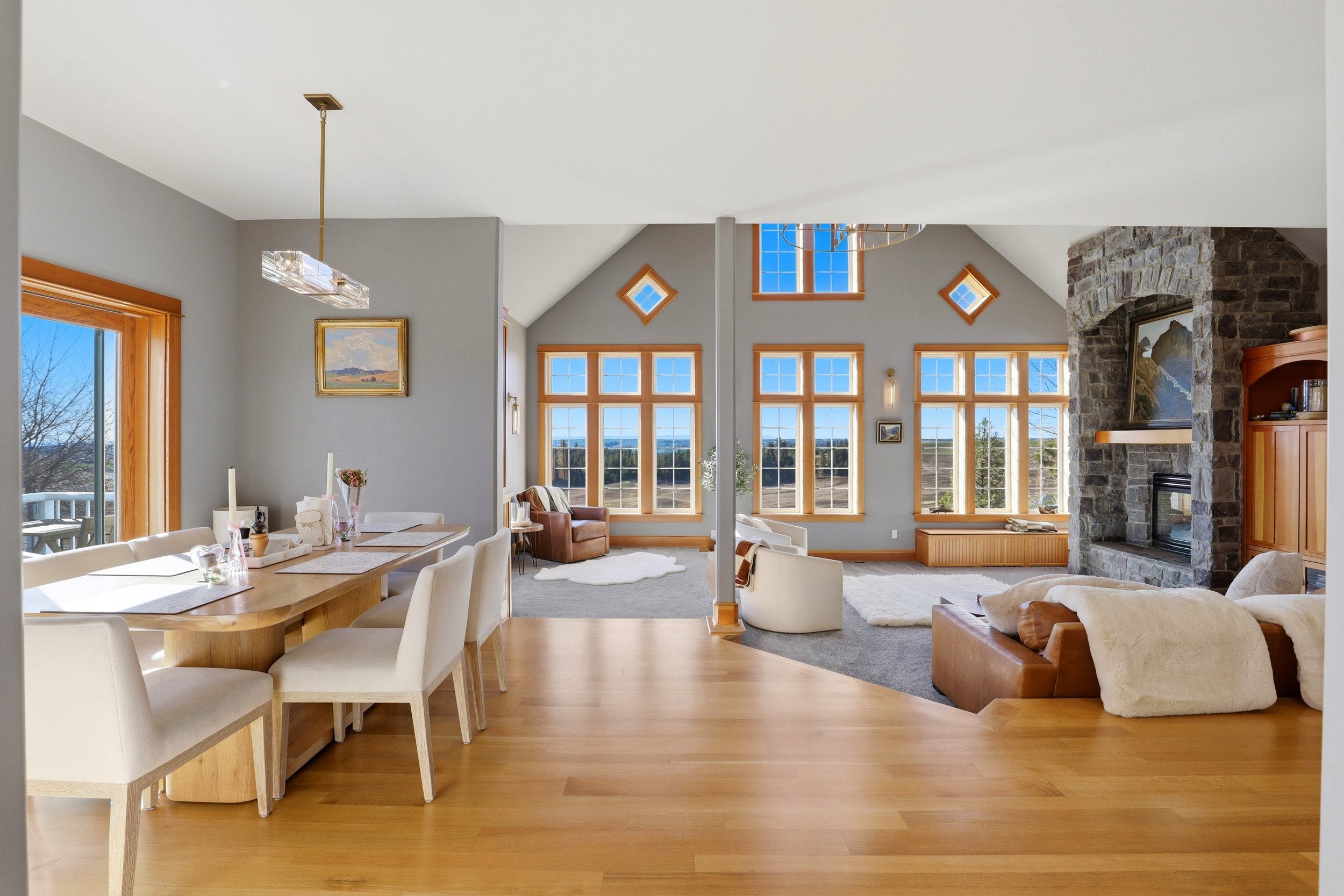 Spacious living and dining area with large windows, stone fireplace, and wooden accents.