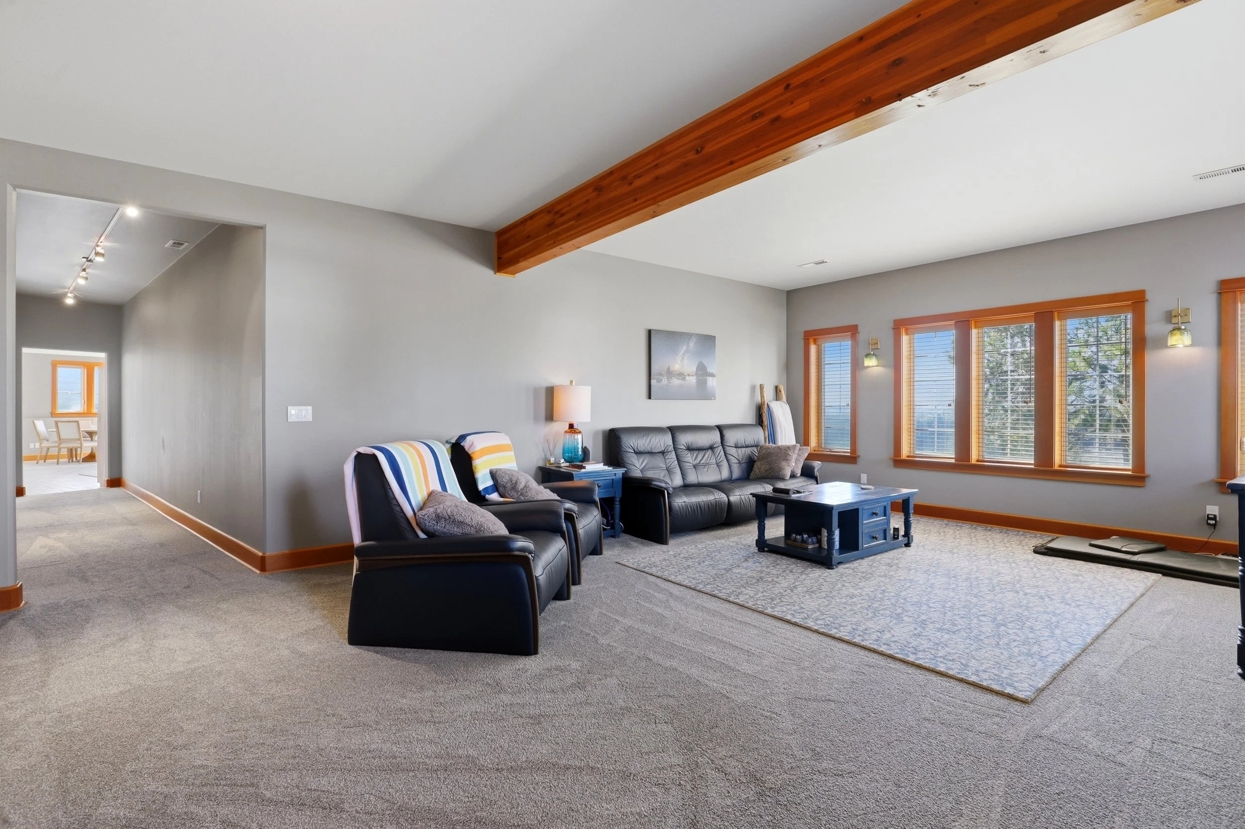 Living room with gray walls, large windows, black leather sofa, armchairs with striped blankets, coffee table, area rug, and wall art. Adjacent dining area visible in the background.