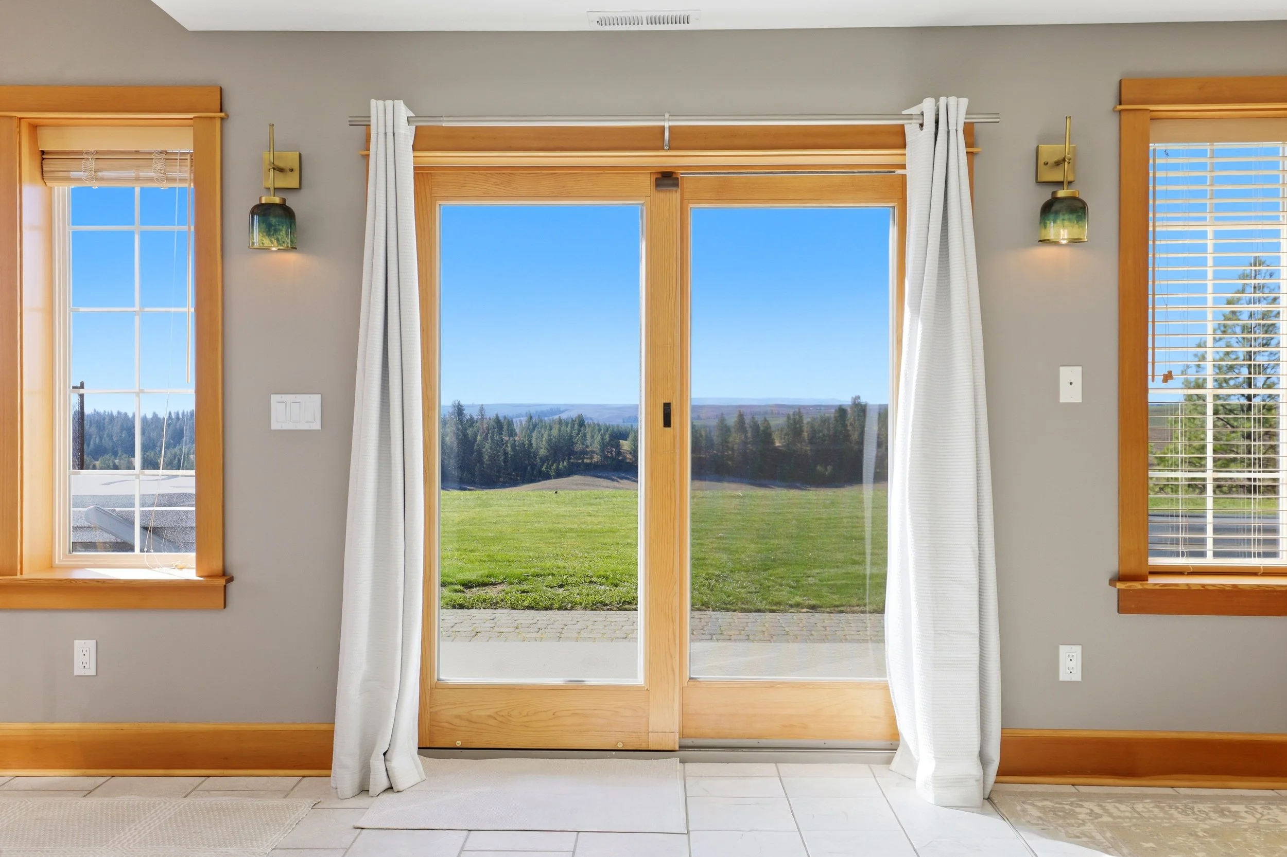 View of a kitchen door with large glass panes, white curtains, and outdoor scenery including green grass and trees.