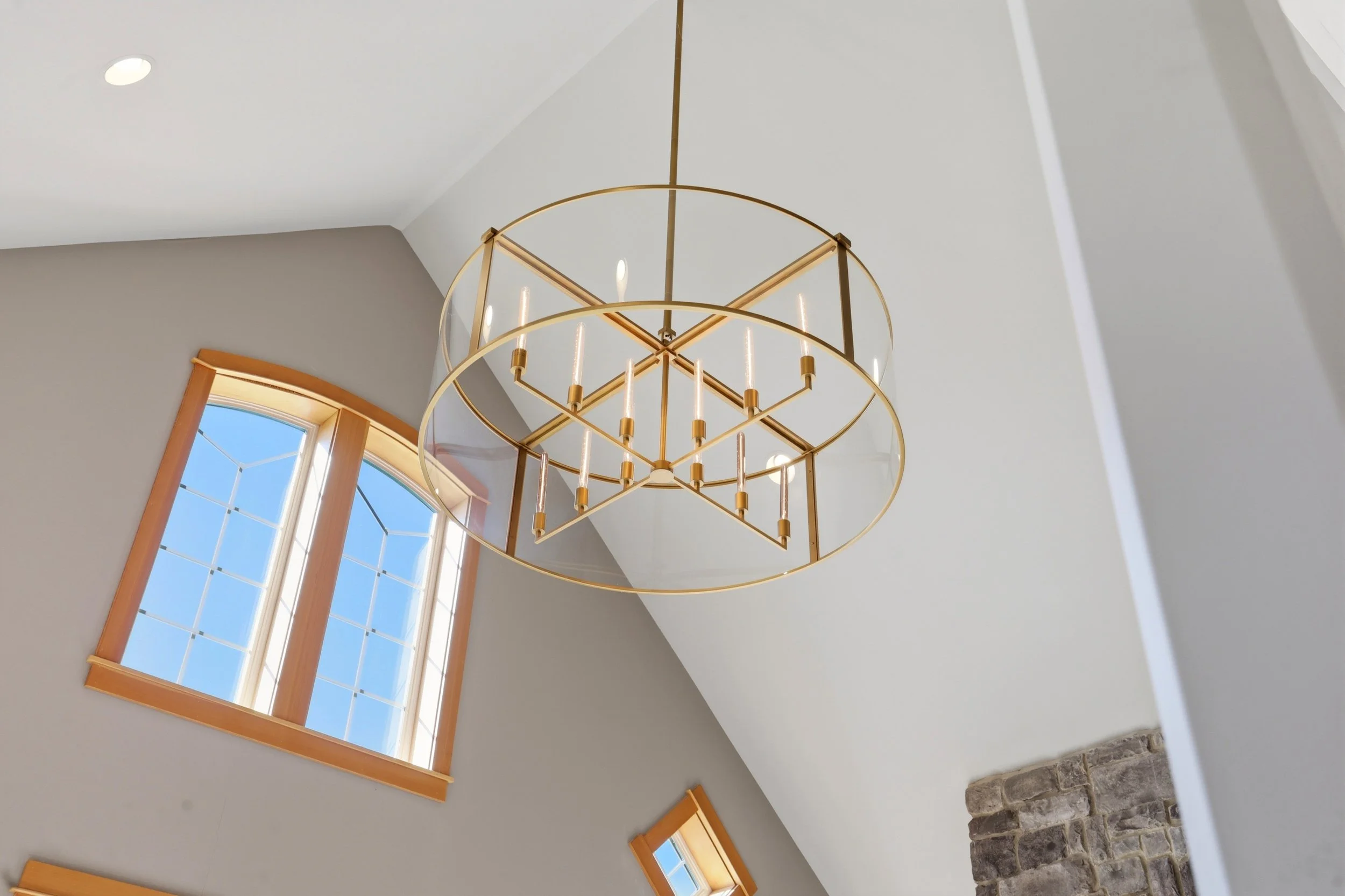 A gold chandelier hanging from the ceiling with no visible bulbs, in a room with large window and white walls.