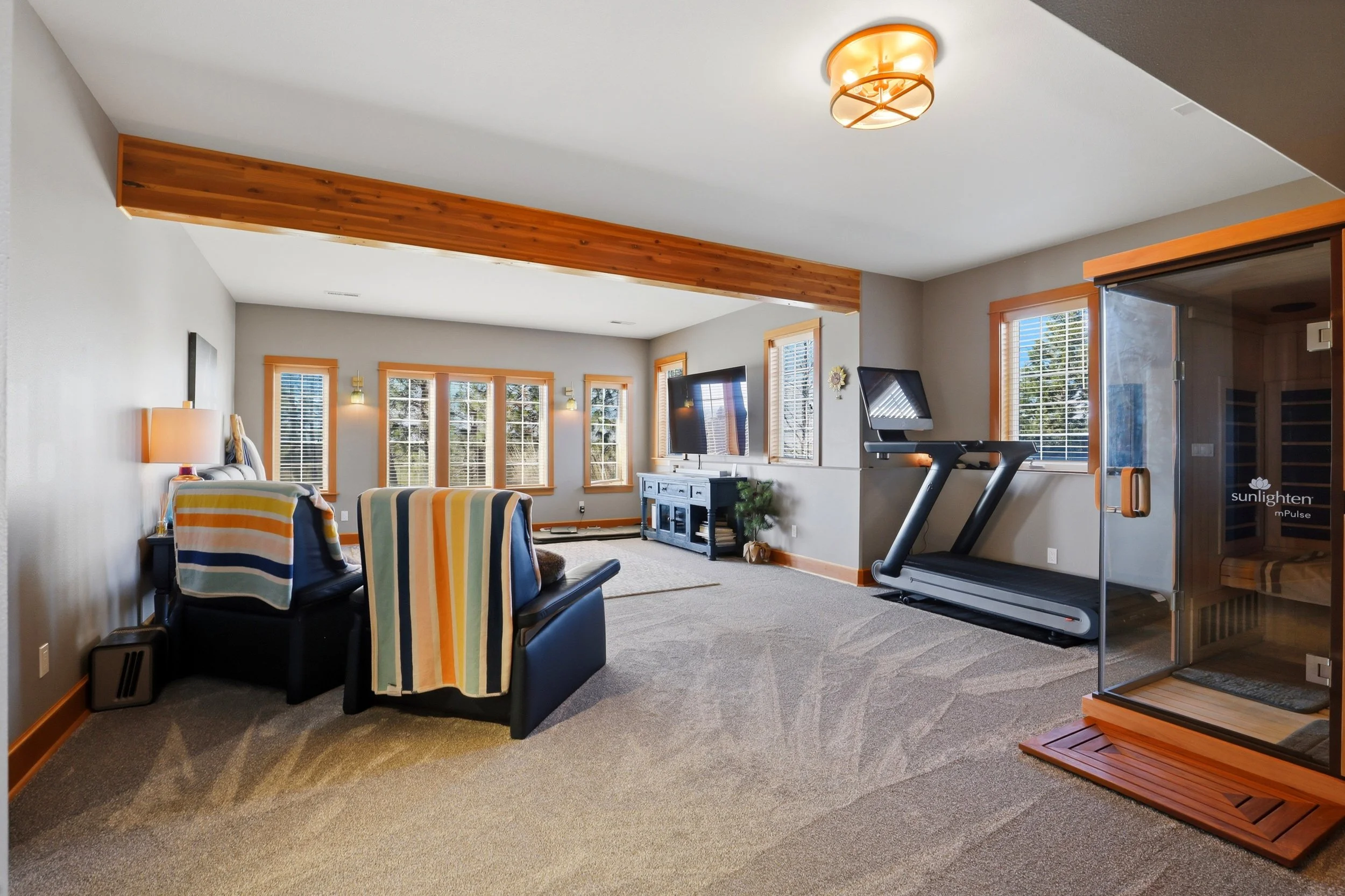 Living room with striped chairs, large windows, a flat-screen TV, a treadmill, and wooden accents.