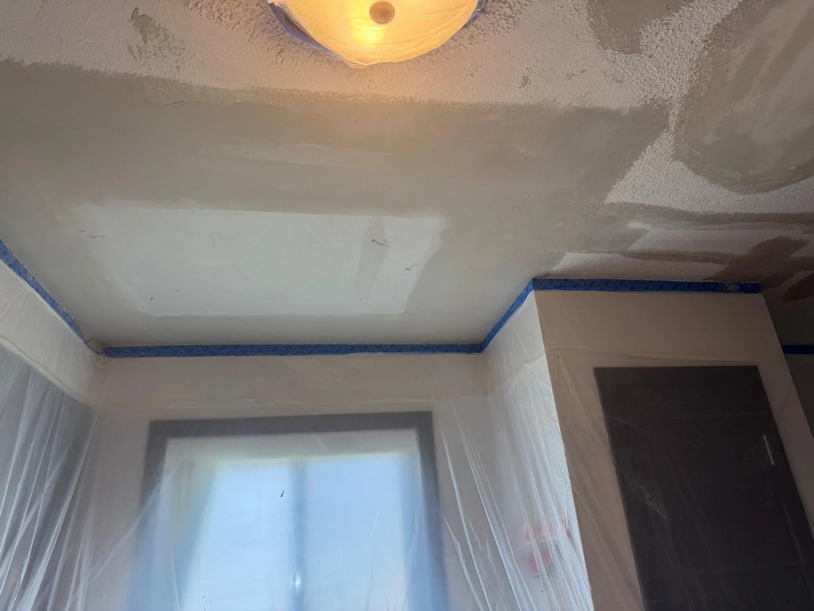 A room under renovation with a textured ceiling, partially painted walls, photo taken upside down, with a window letting in natural light, and a heater or appliance on the right side.