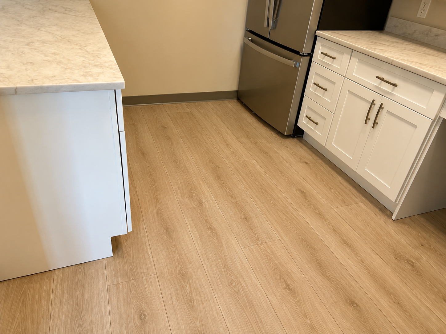 Kitchen corner with white cabinets, marble countertops, stainless steel refrigerator, and wood-look flooring.