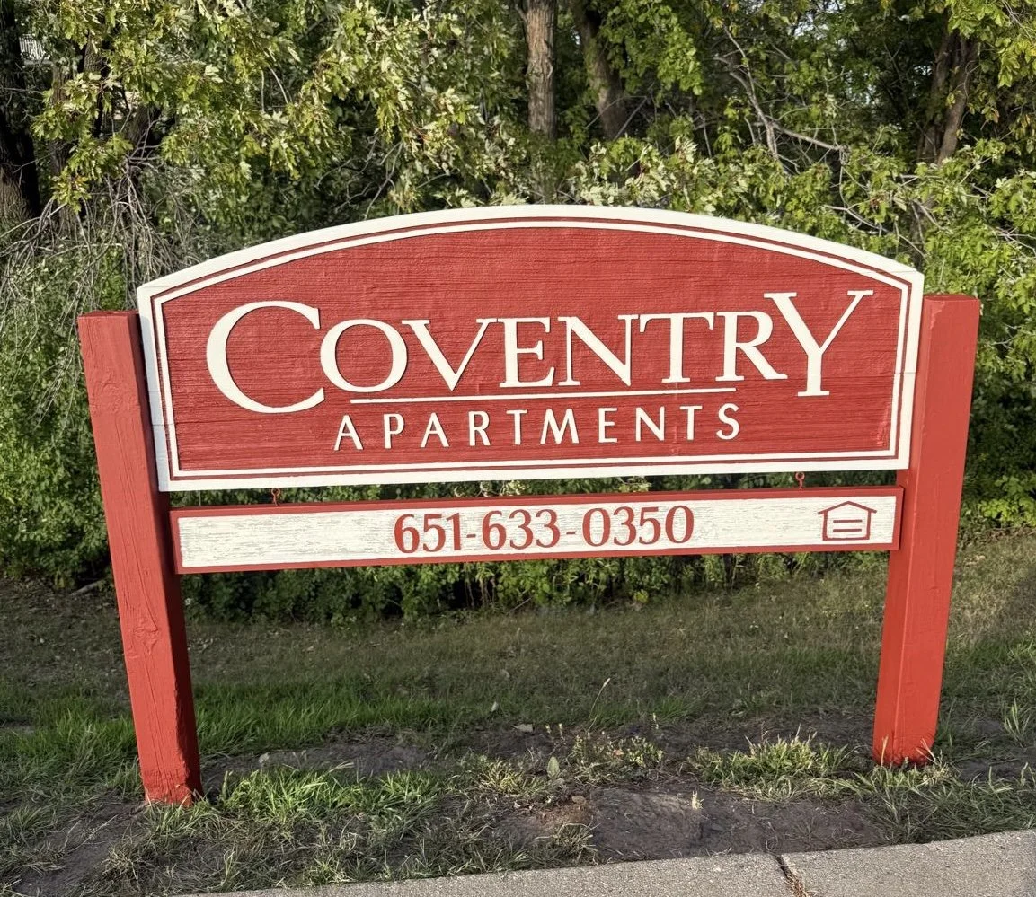 Sign for Coventry Apartments with phone number 651-633-0350, red and white sign outside with trees in the background.