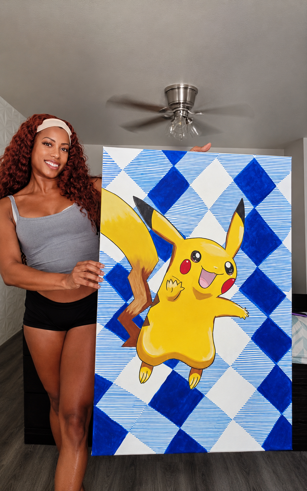 A woman with curly red hair and a white headband holding a colorful painting of Pikachu from Pokémon, standing in a room with a ceiling fan.