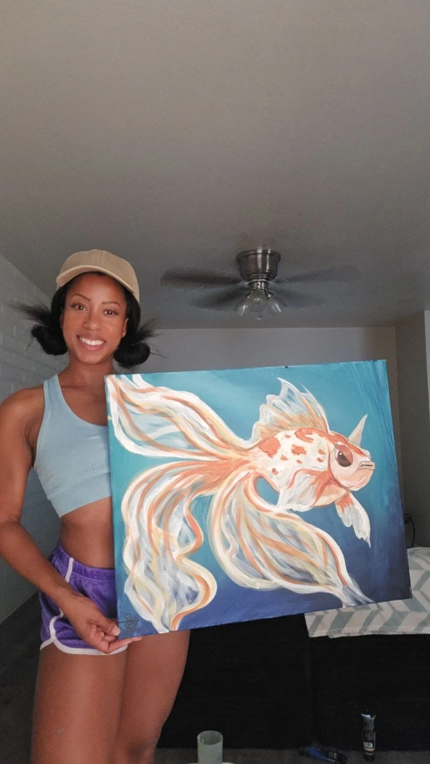 A woman smiling and holding a painting of a colorful fish with flowing fins.