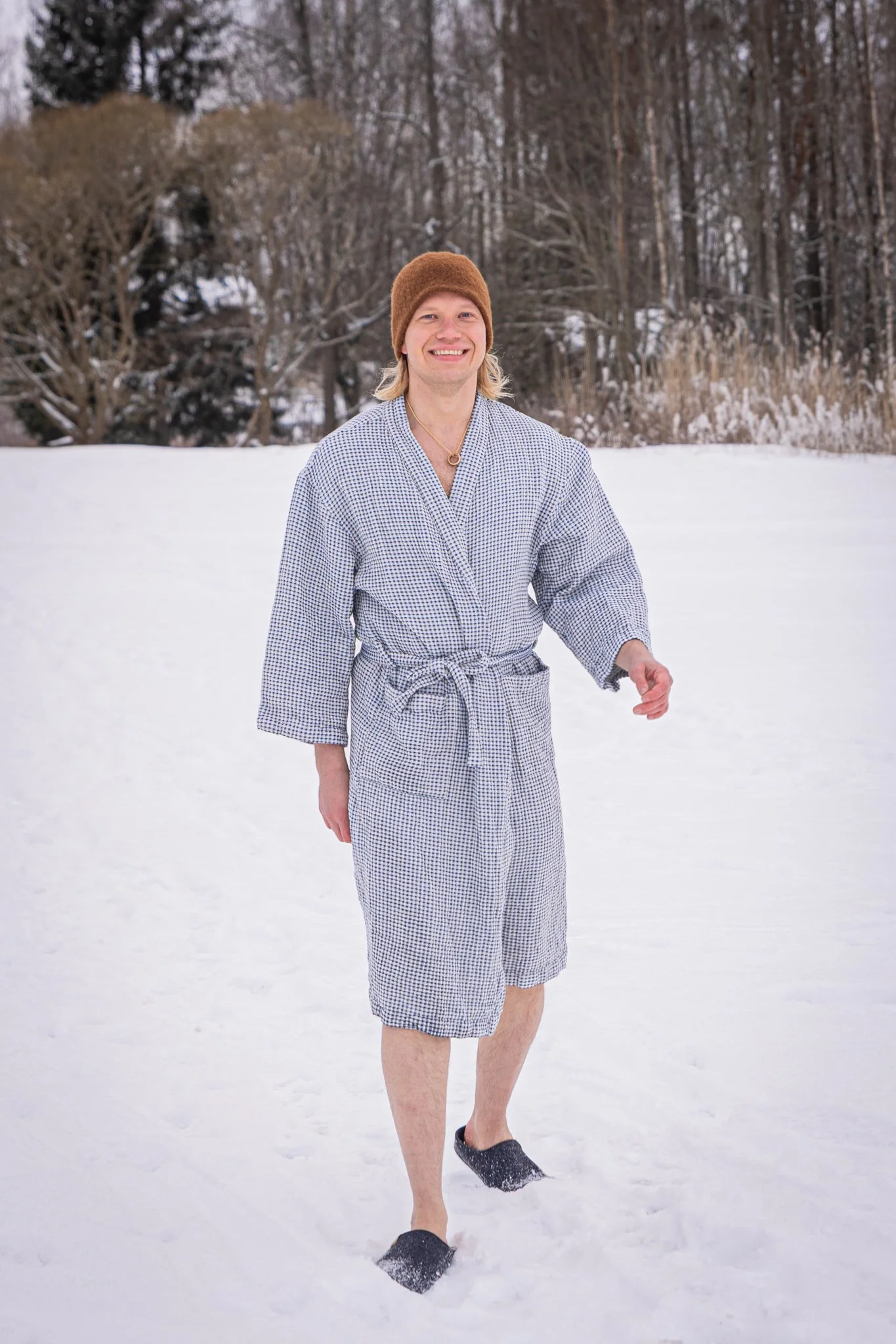 Aleksi Virtanen walking on ice in Strömma, Finland. Sauna hat, jewelry and a robe.
