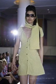 Fashion model walking down runway in yellow polka dot dress and sunglasses
