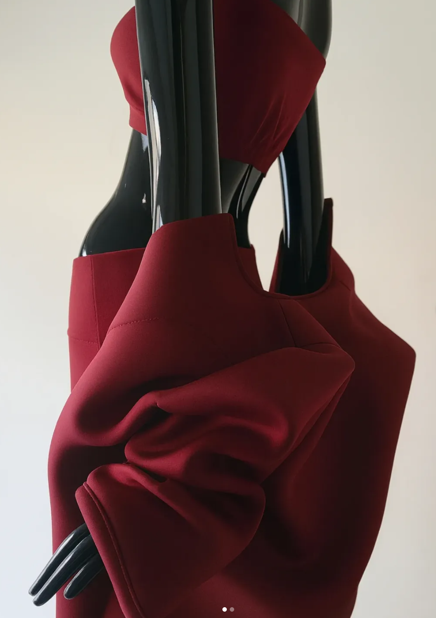 Close-up of a black mannequin wearing a red long-sleeve top or dress, with their hand resting on their arm.