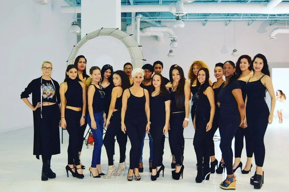 Group of women dressed in black standing in a studio with white walls and industrial ceiling, posing for a photo.