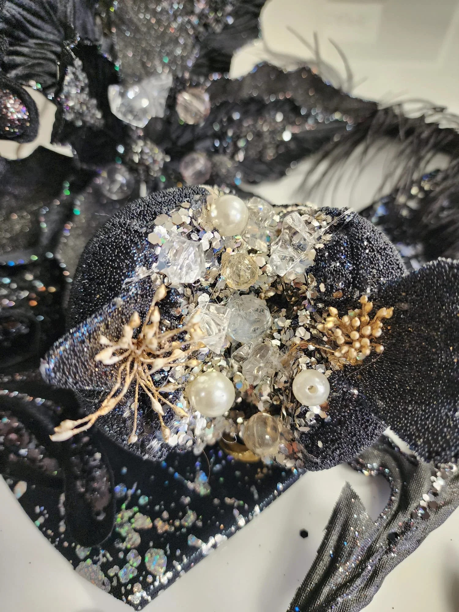 Close-up of a black embellished fabric with shiny beads, pearls, and rhinestones, and a black mesh fabric with iridescent glitter.