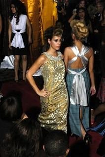 A woman in a gold and silver dress standing on a stage or runway during a fashion event.