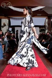 A woman walking on a runway in a black, white, and blue patterned dress during a fashion show.