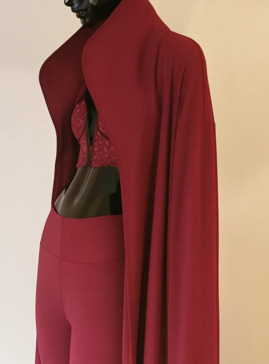 Red mannequin wearing a matching set of red leggings, a lace bralette, and a long red cape.