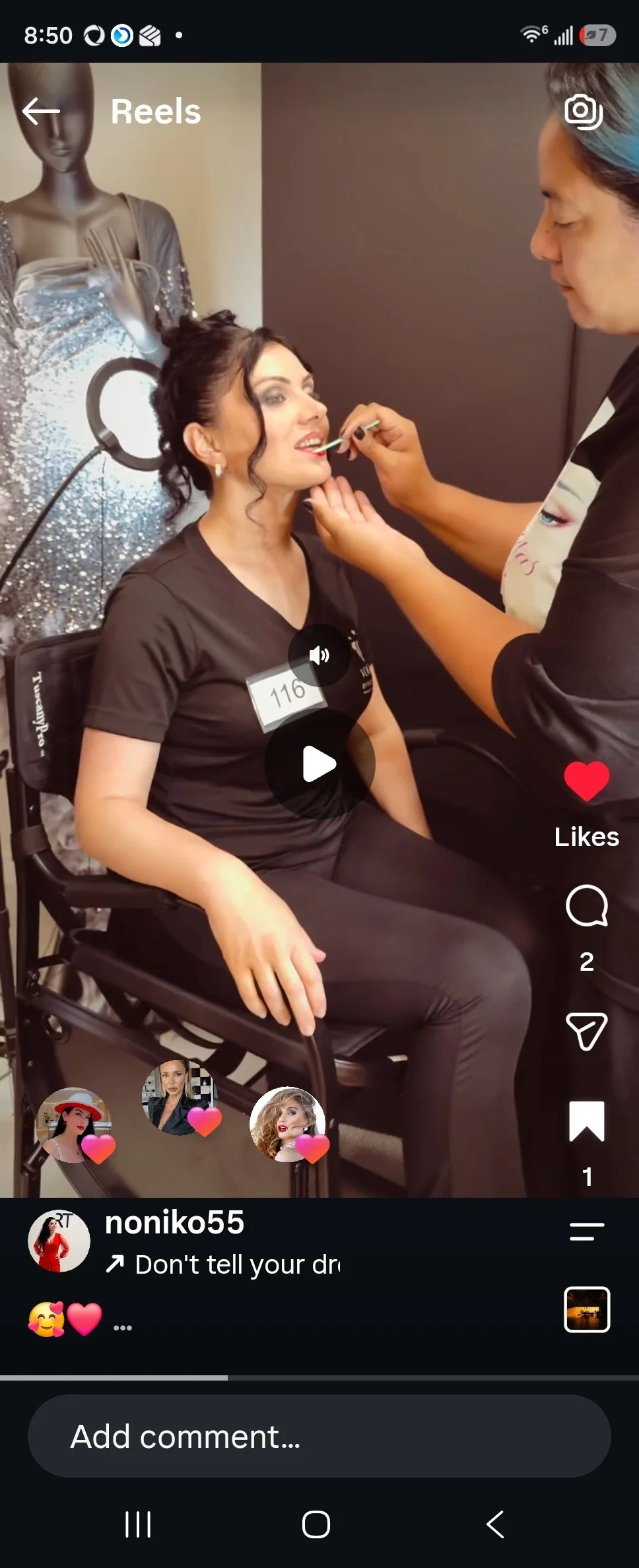Woman sitting in a chair receiving makeup application from a makeup artist, with a mannequin in the background.