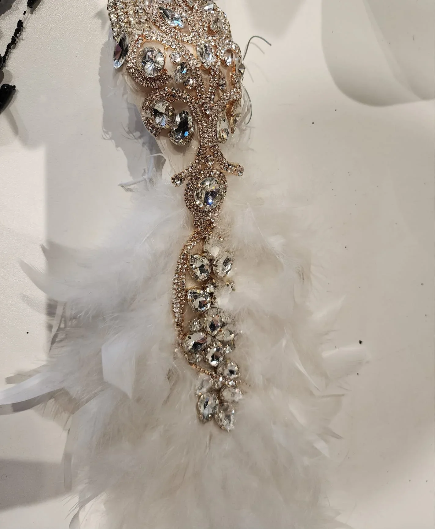A decorative item with large clear rhinestones arranged in a floral pattern, accented with feathers and a gold-colored base.