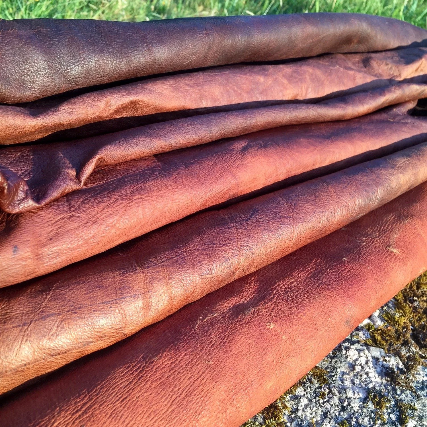 Close-up of several folded rolls of brown leather outdoors on a rocky surface.