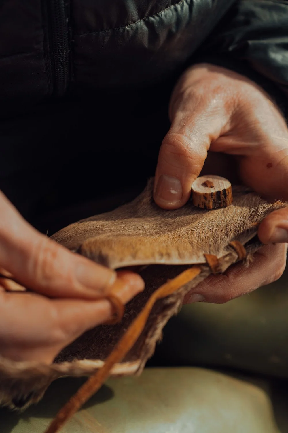 Close-up of a person's hands applying a wooden button to the fur of a small animal, with a leather strap nearby.