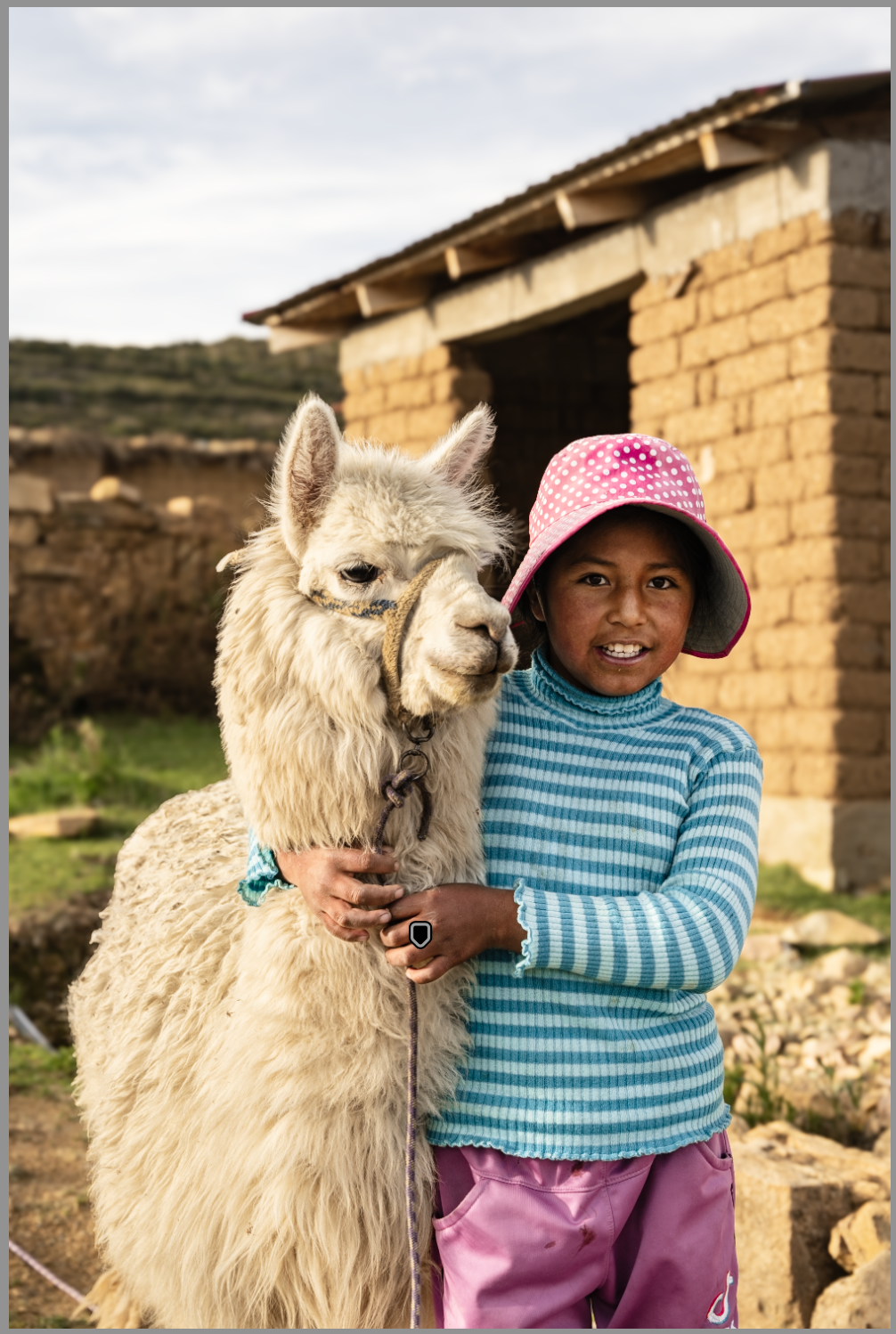 A young girl holding a llama outdoors, with a rustic building in the background.