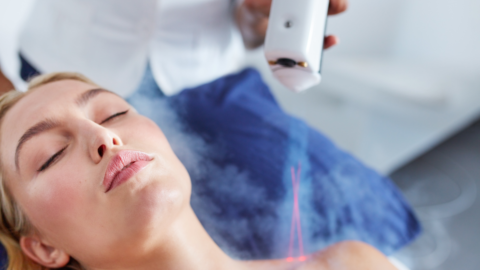 A woman lying down with her eyes closed, receiving laser skin treatment on her face from a medical professional.
