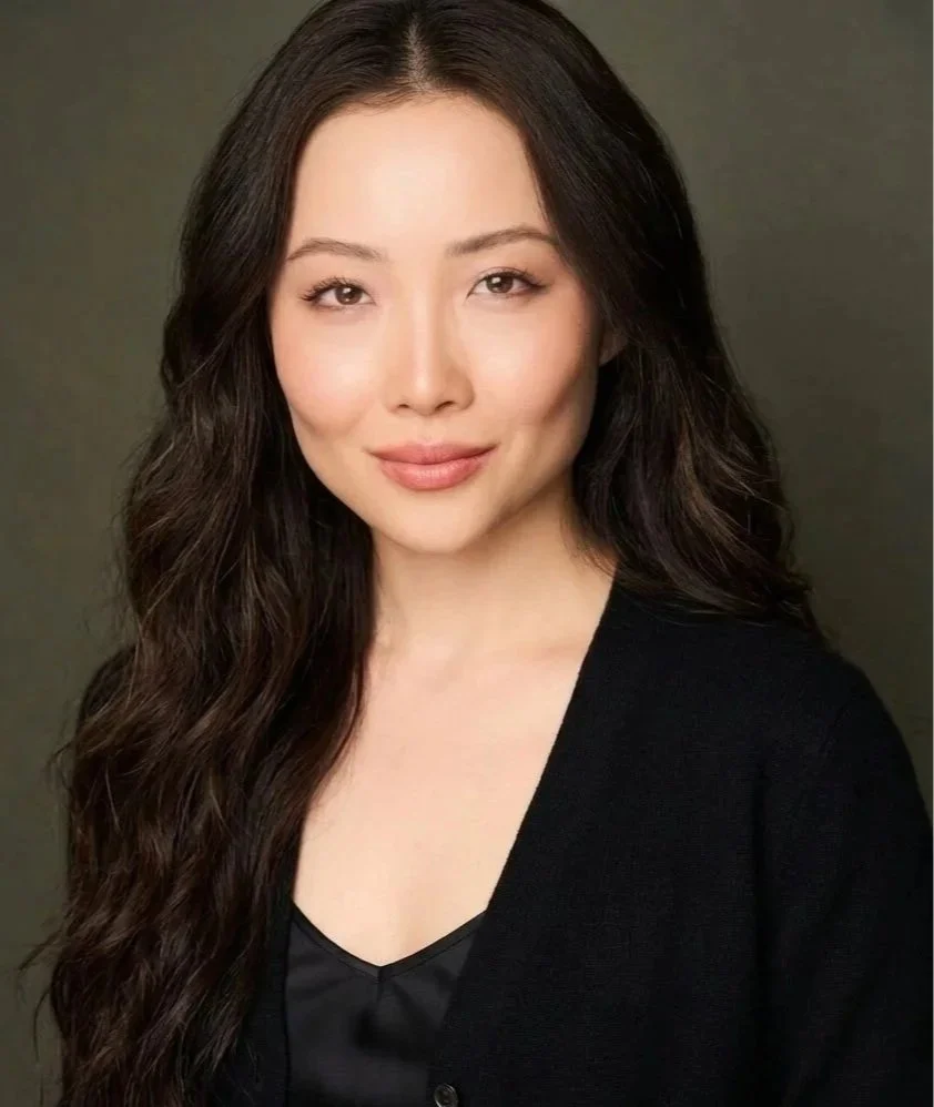 Jadene Meyer, an actress with long, wavy dark hair wearing a black top and blazer, posing against a plain background. As featured on Meyer Studios jadenemeyer.com.