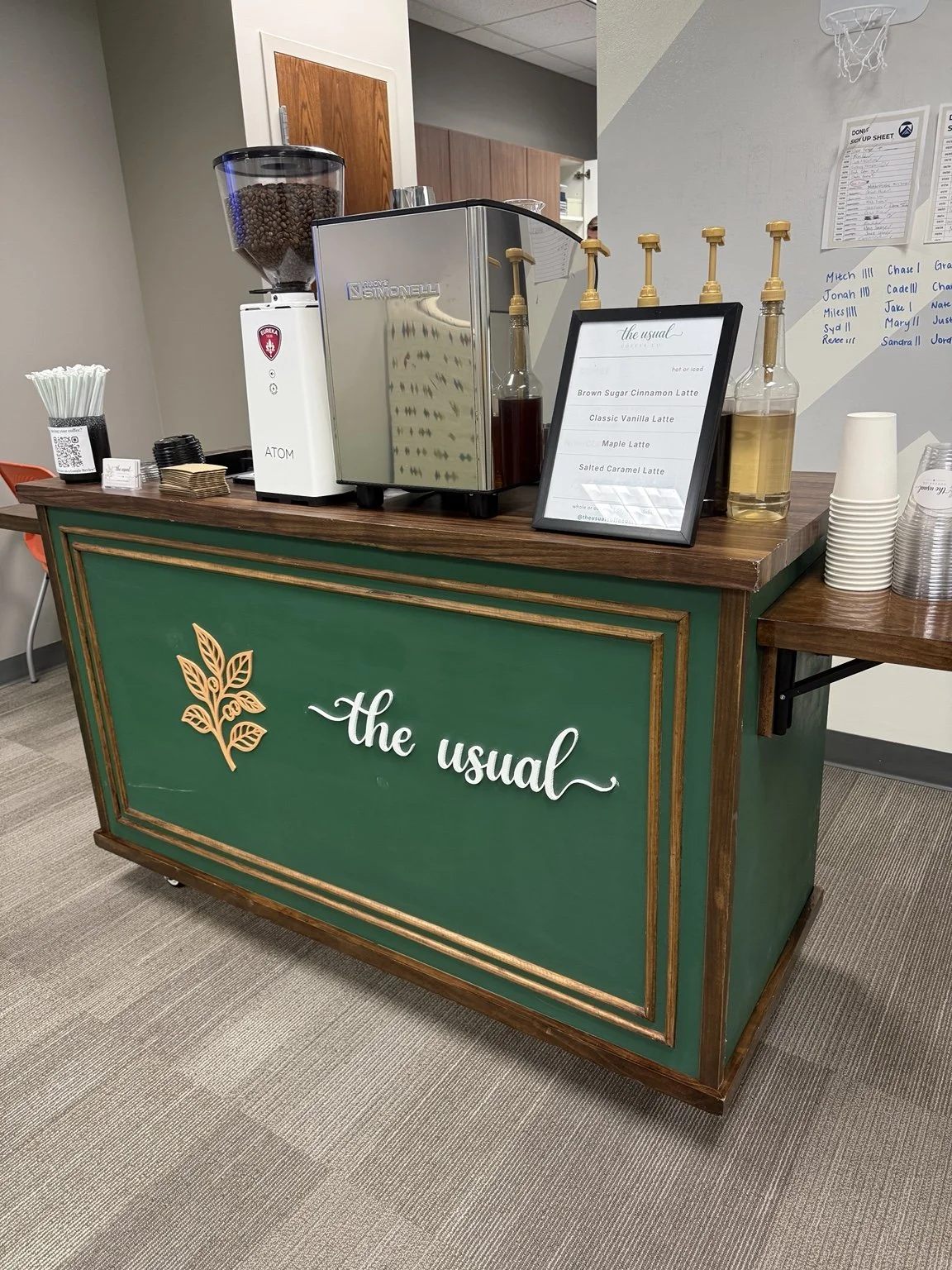 The Usual Coffee Co. green and gold mobile espresso cart set up indoors with an espresso machine, syrups, and a menu.