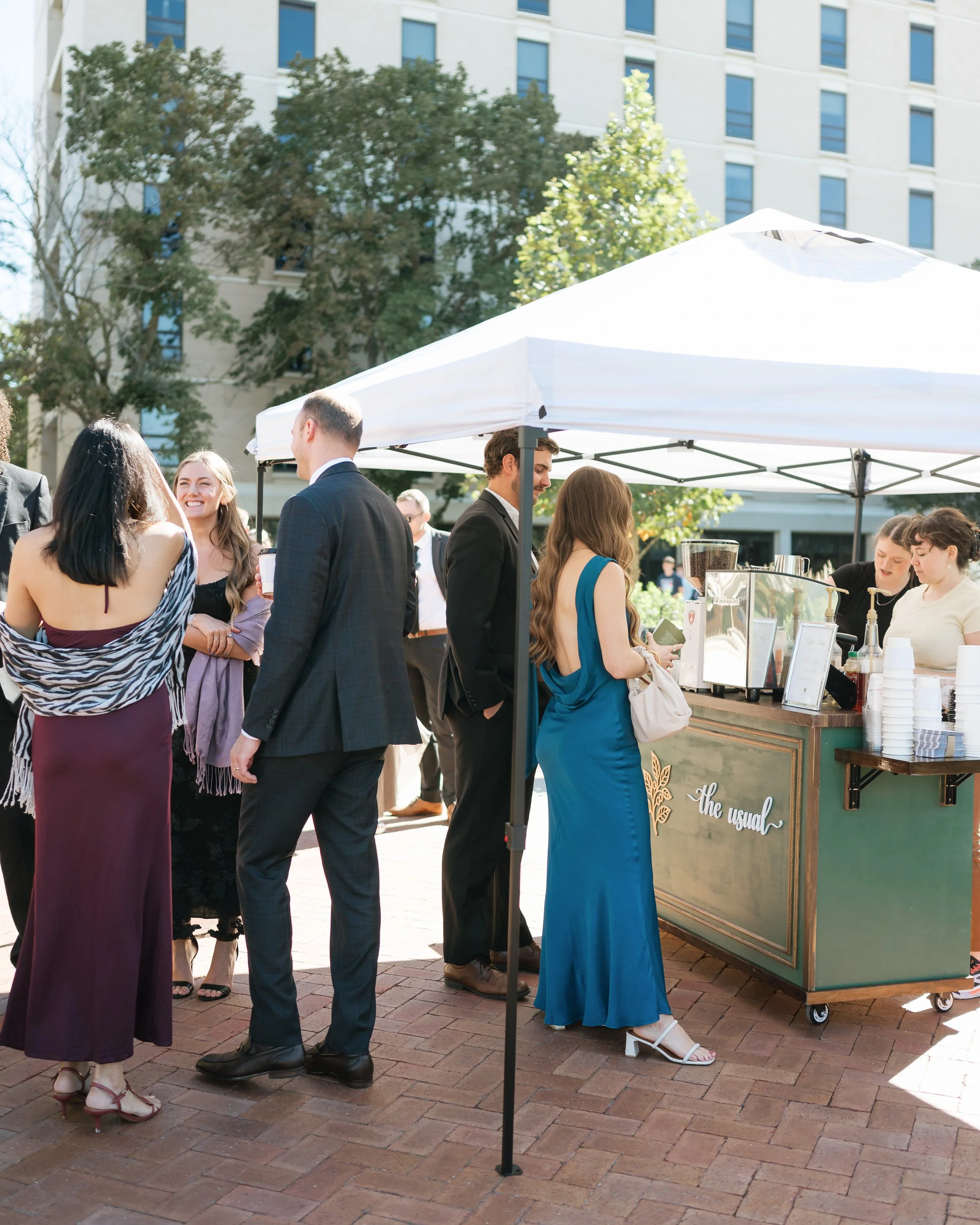Wedding guests gathered around The Usual Coffee Co. espresso cart beneath a white canopy.