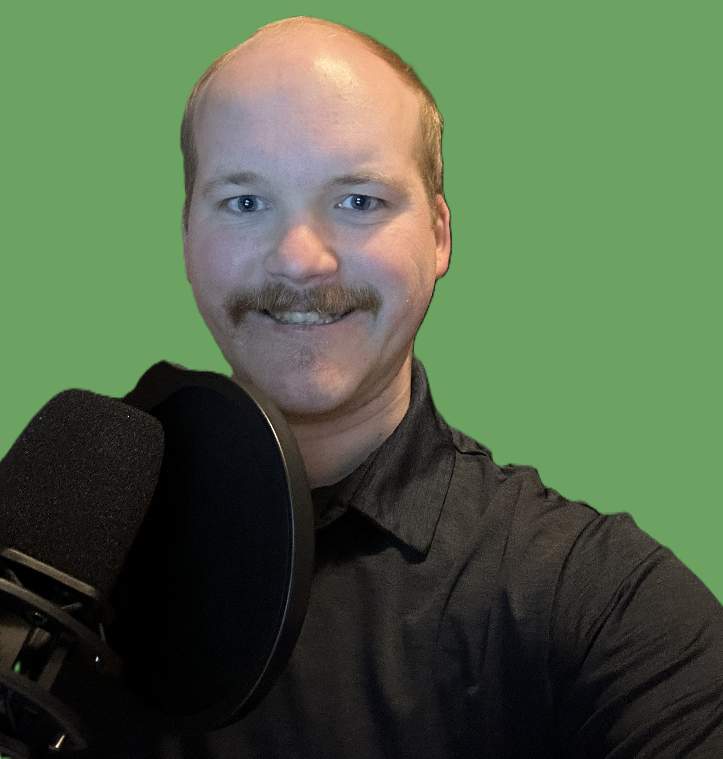 A man with a light complexion, blue eyes, a beard, and a mustache, smiling at the camera, in front of a green background, wearing a black sweater, and seated near a microphone.