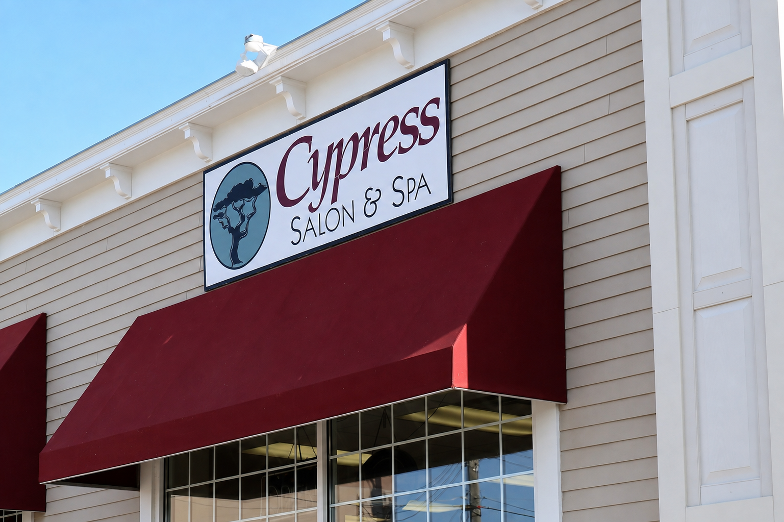 Exterior of Cypress Salon & Spa with a white sign, maroon awnings, and a large window.