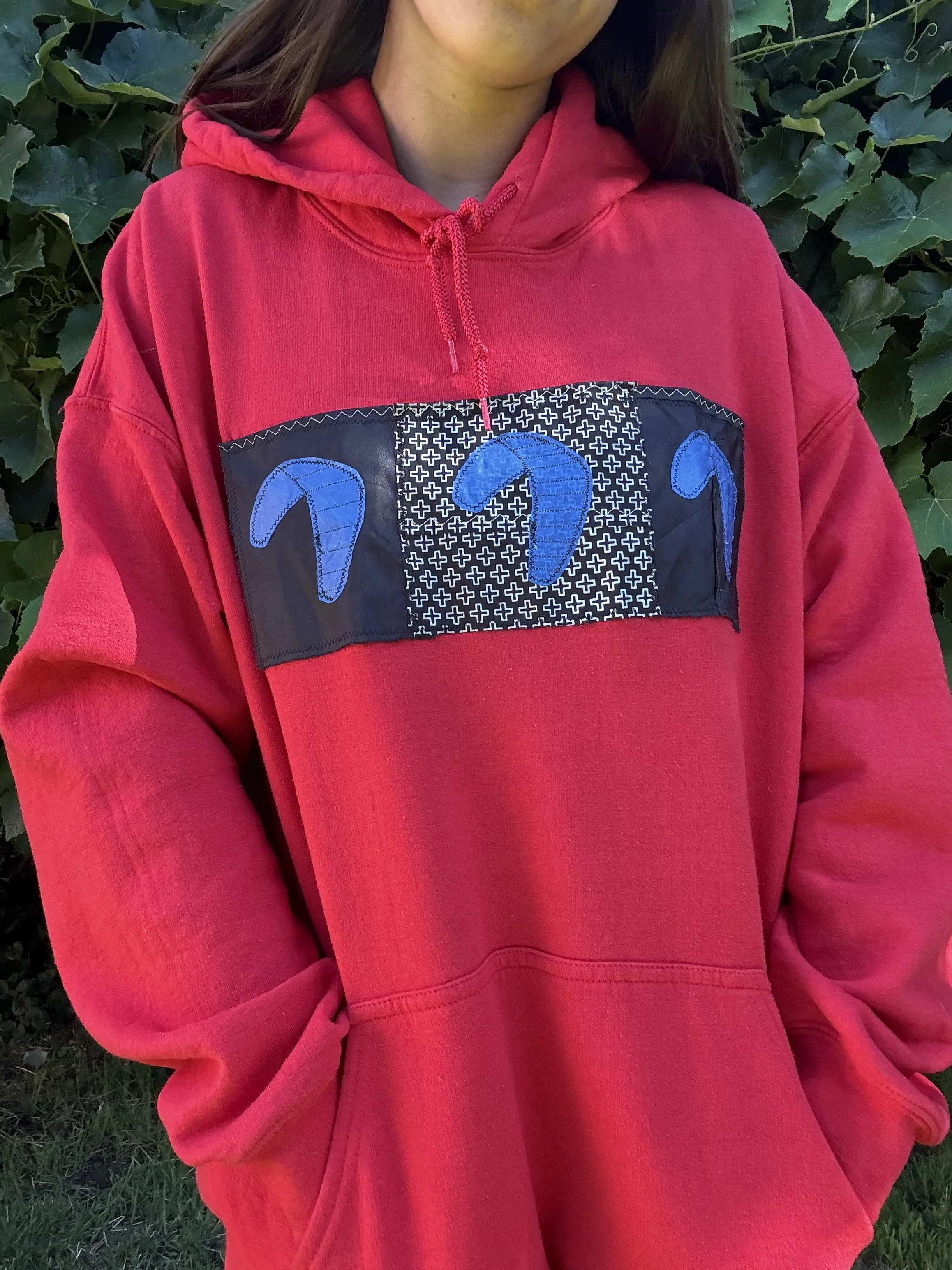 Close-up of a person wearing a red hoodie with a black patch featuring blue sewing patches in the shape of kites from kiteboarding