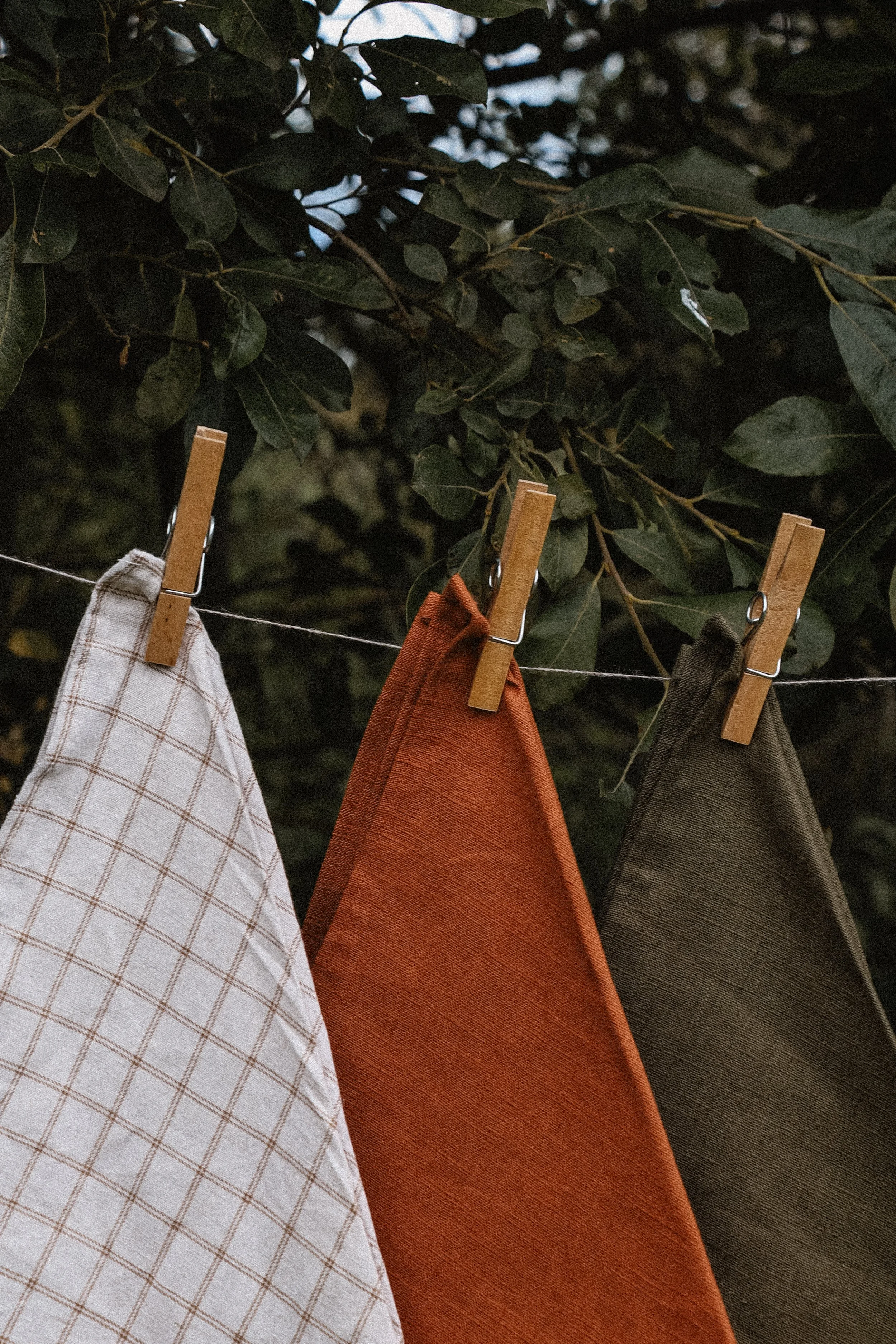 Linen Bread Bags hanging on a clothesline with clothespins, in front of dense green foliage.