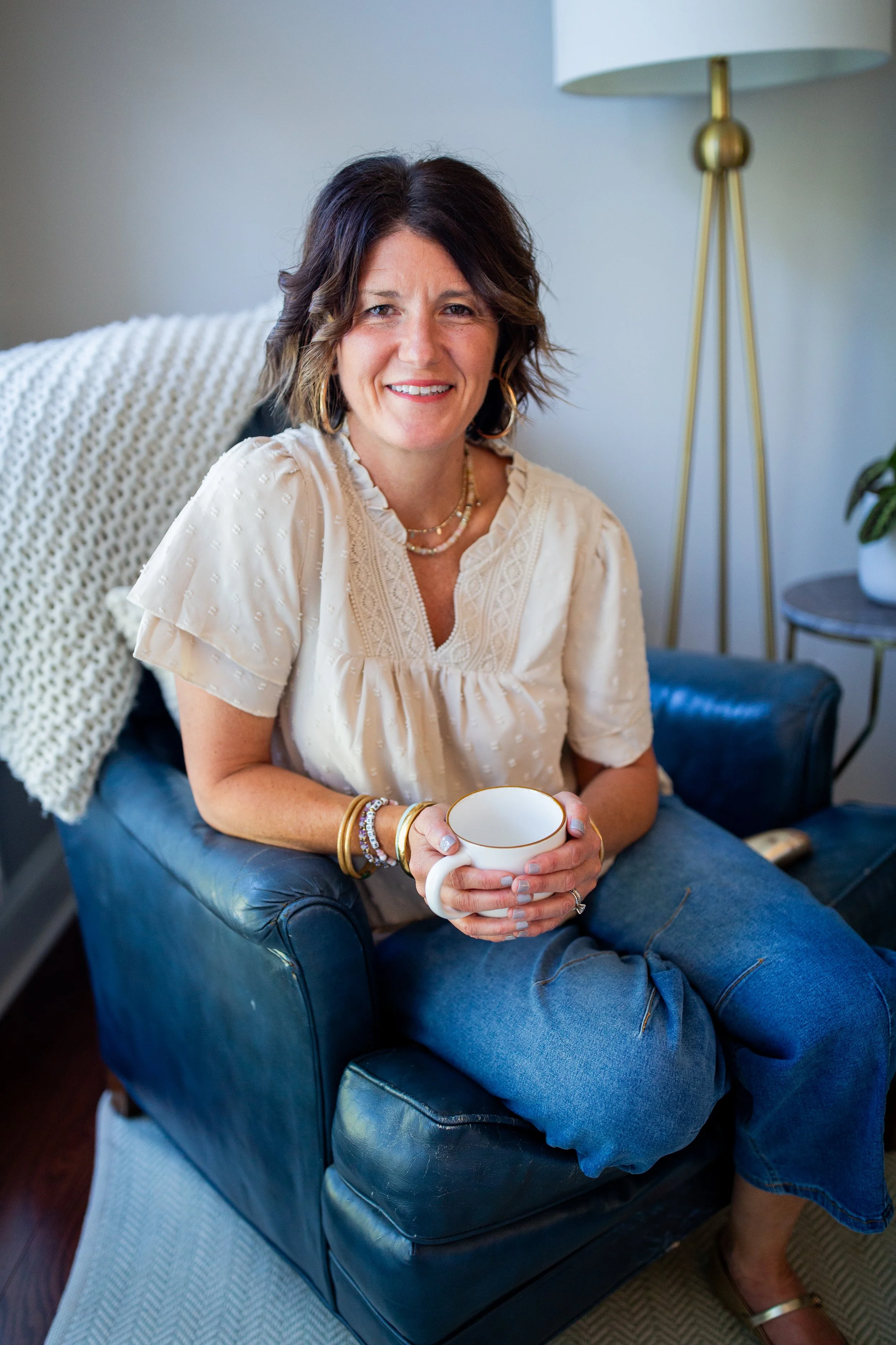 Smiling woman in a white blouse sitting in a blue chair and holding a coffee cup