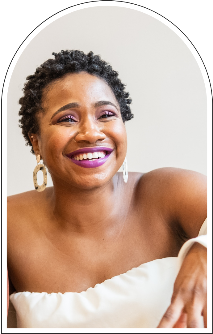 Smiling Black woman with short curly hair, purple lipstick, statement earrings, and an off-the-shoulder white top