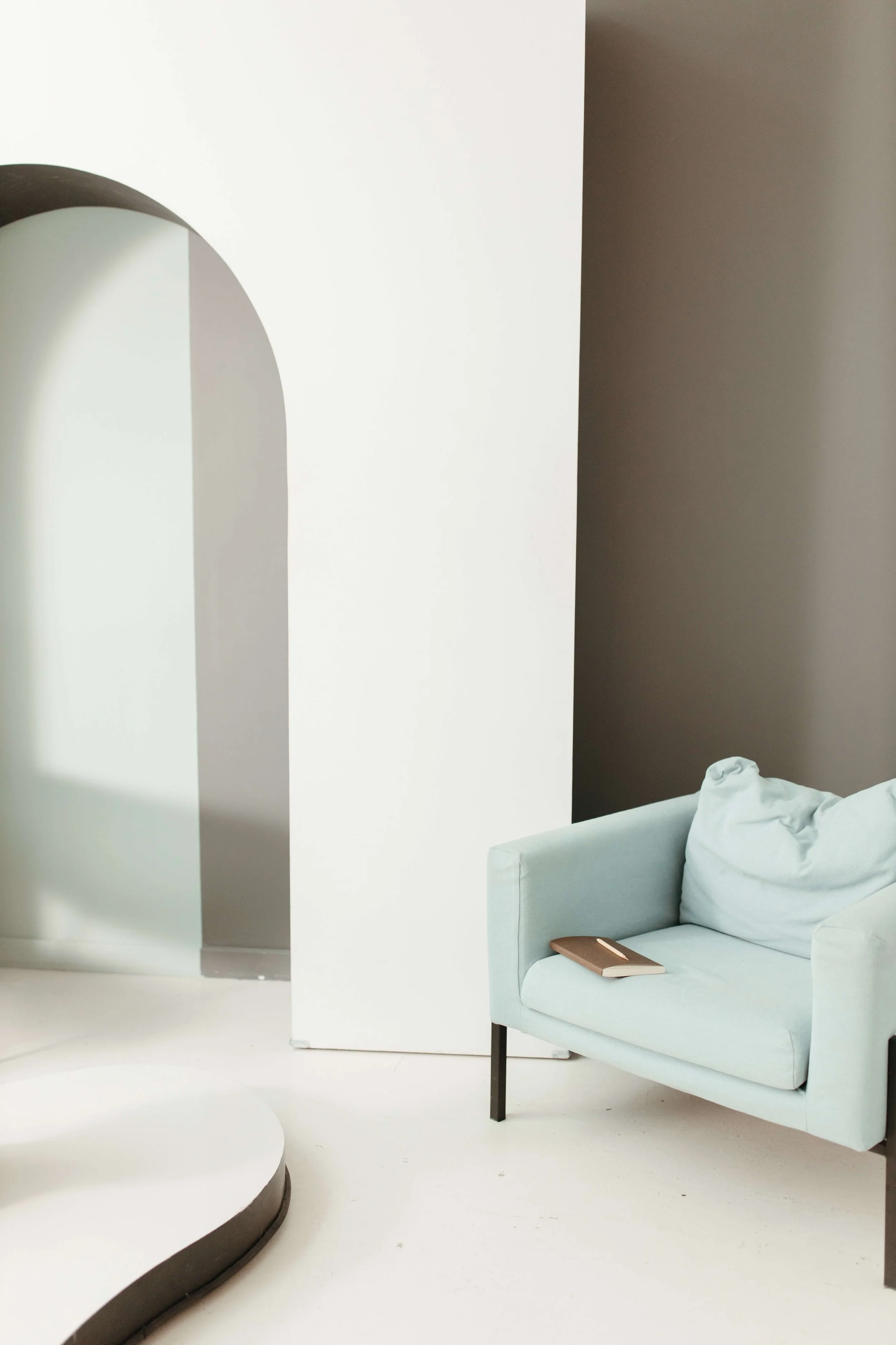 Modern minimalist living room with a light blue sofa, book, white round coffee table, and curved architectural wall